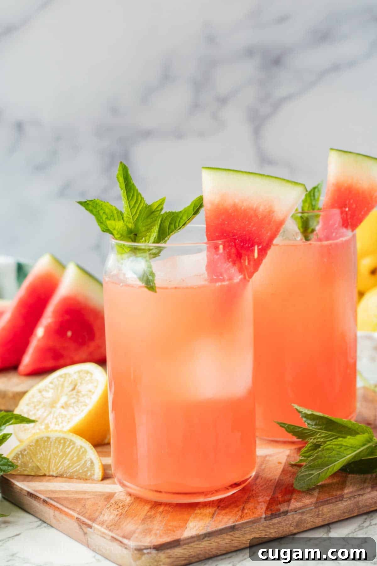 Glass of watermelon mint lemonade on wood cutting board with slice of watermelon and sprig of mint on top.