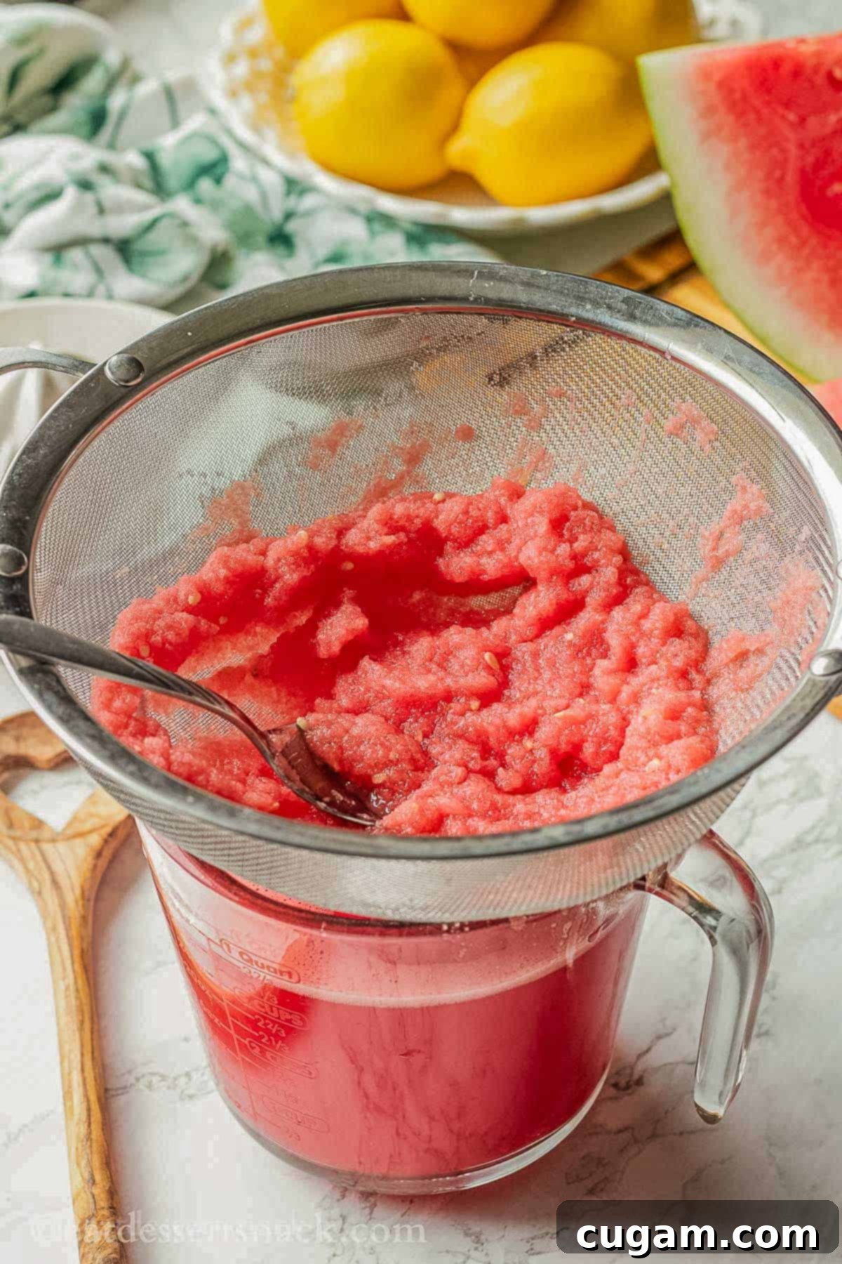 Straining watermelon juice through a seive into a glass measuring cup.