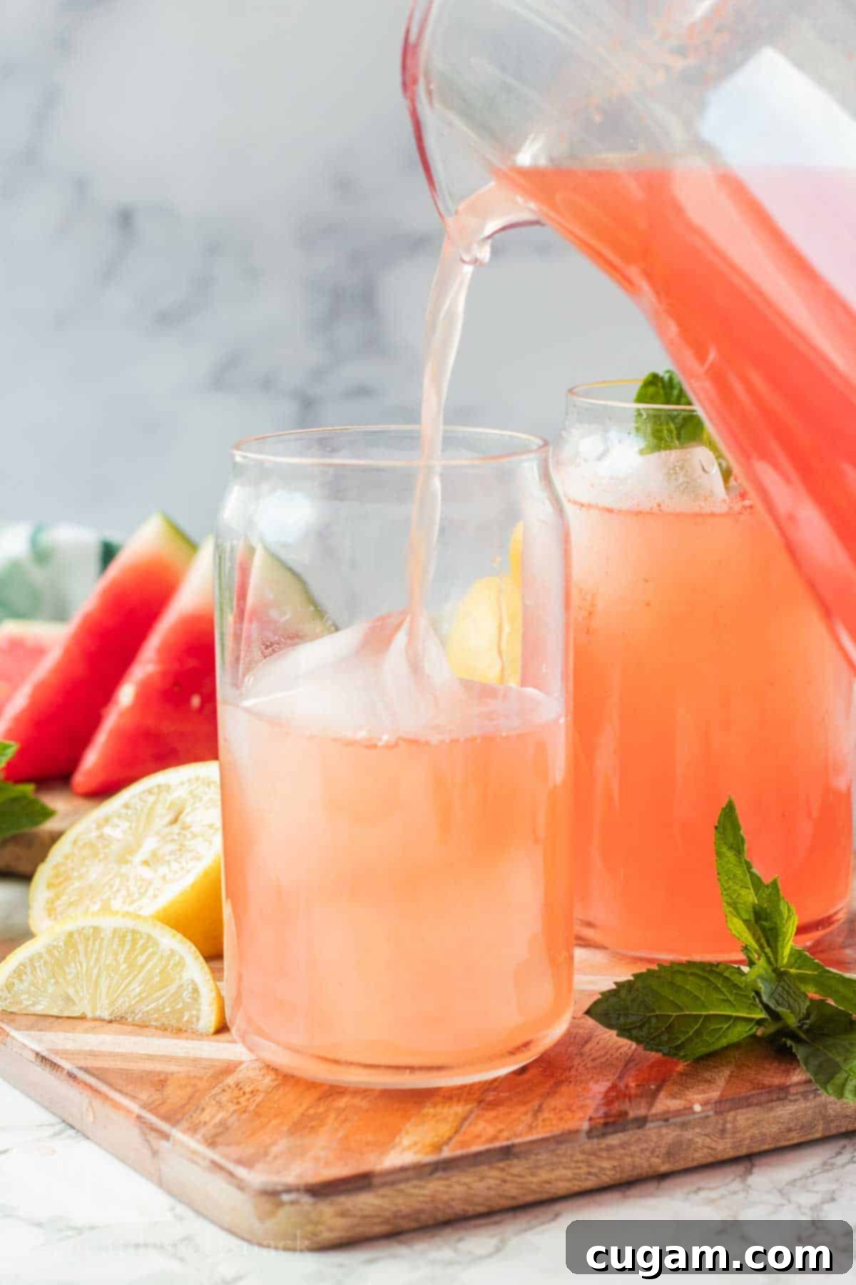 Pouring watermelon lemonade into a clear glass on a cutting board.