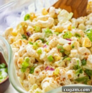 A tantalizing image of Deviled Egg Macaroni Salad, artfully presented in a clear glass bowl with wavy edges, garnished with a dusting of paprika and fresh green onions on top.