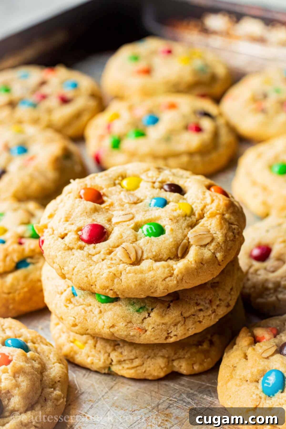 Stack of 3 baked oatmeal m&m cookies on metal baking sheet.