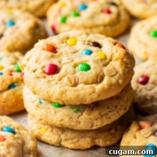 Stack of 3 baked oatmeal m&m cookies on metal baking sheet.
