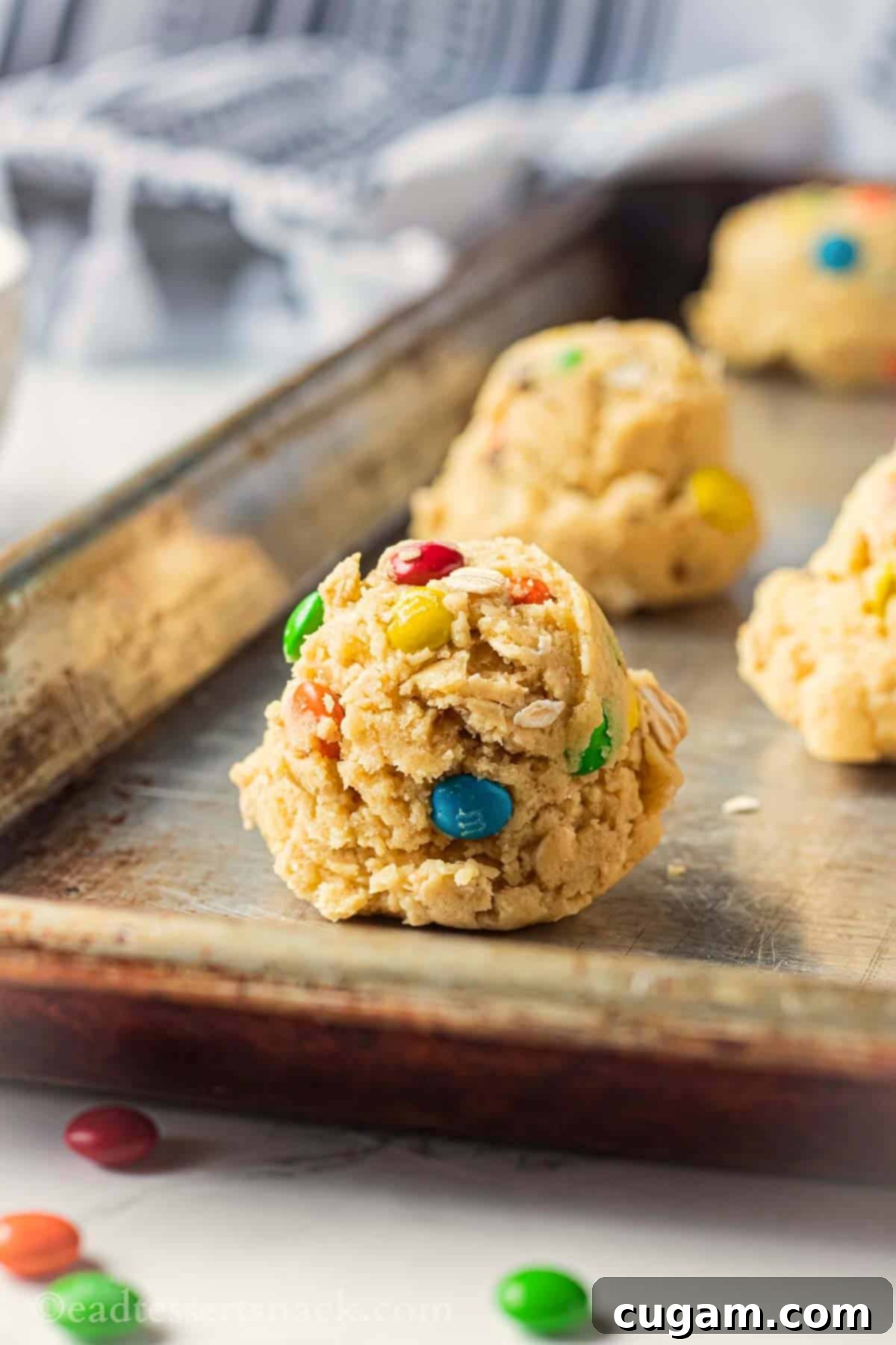 Raw oatmeal m&m cookie dough balls on metal baking sheet.