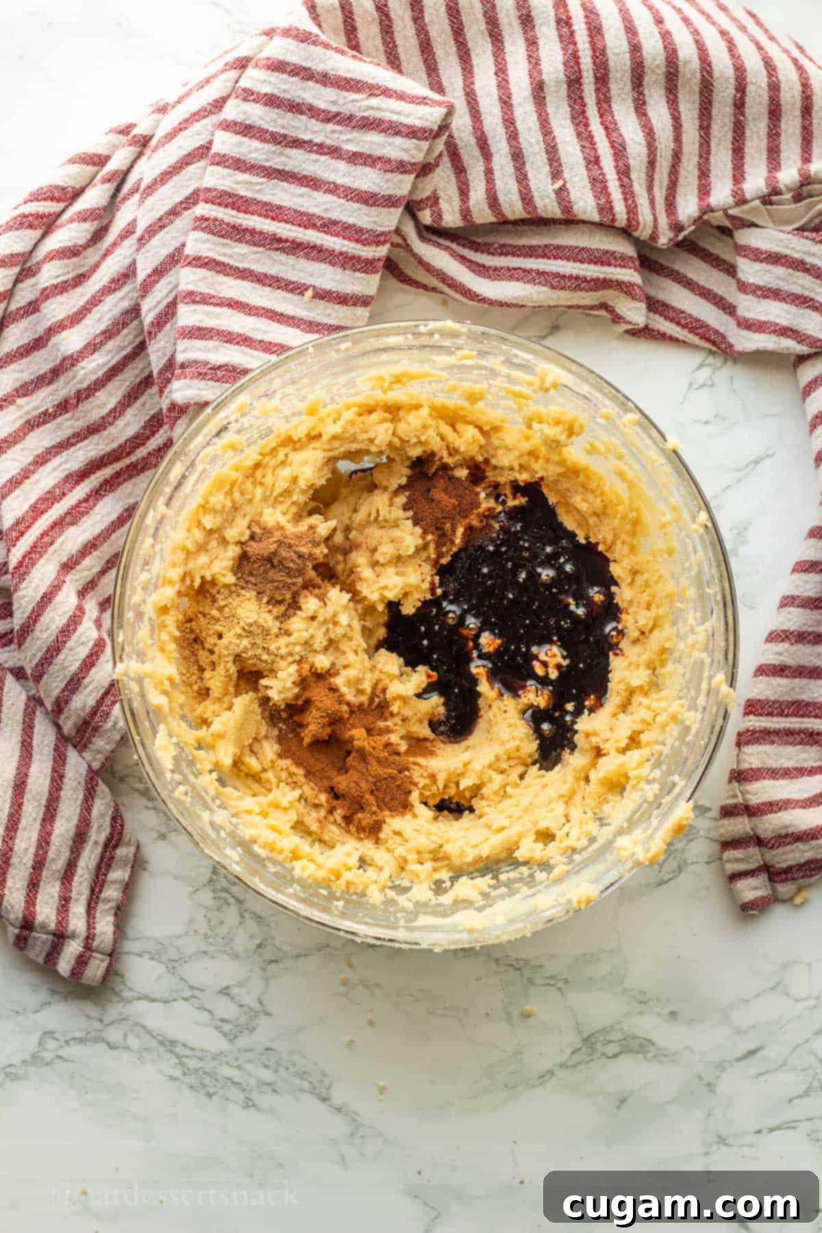 Molasses and spices in butter, sugar, and eggs mixture in glass bowl.