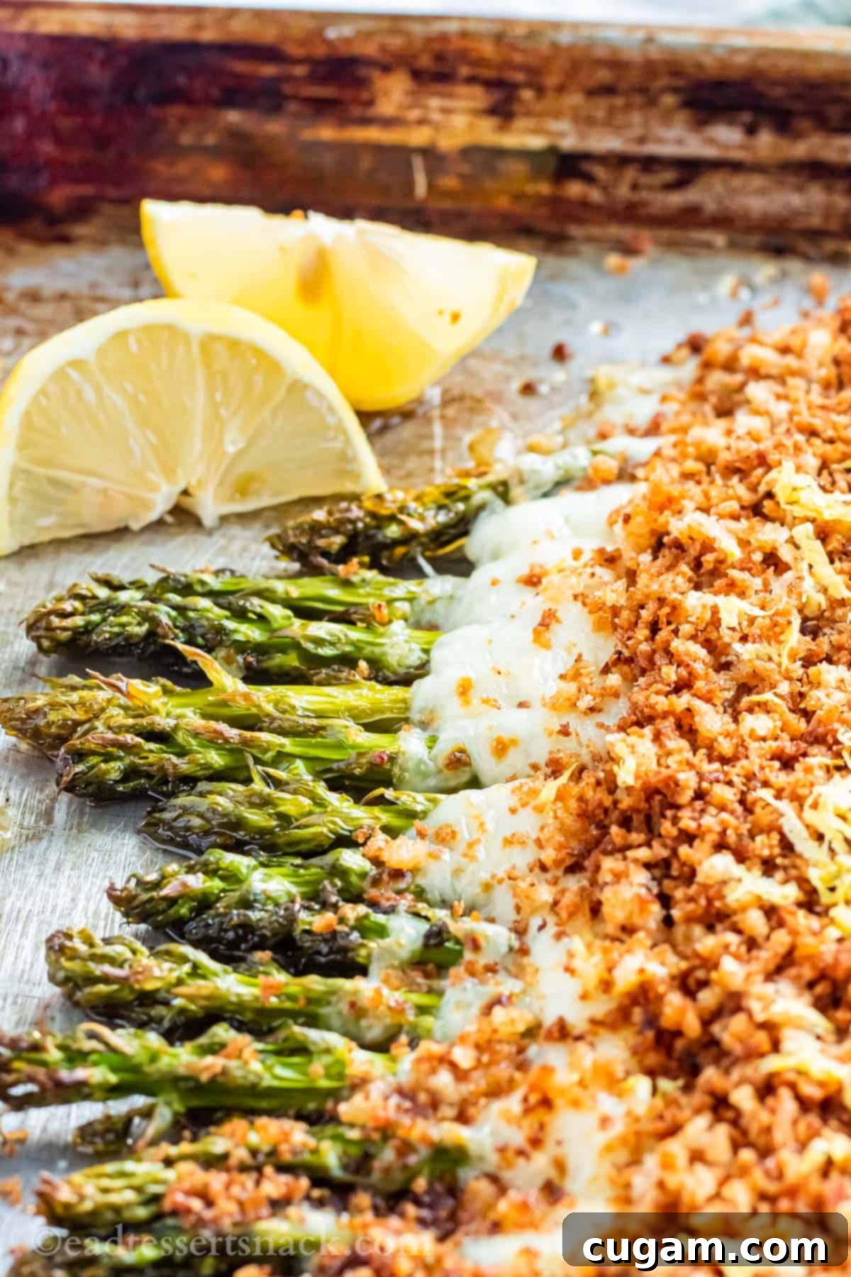 Baked cheesy asparagus with lemon panko breadcrumbs on metal pan, garnished with lemon wedges.