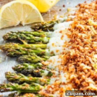Cheesy baked asparagus on metal pan with lemon wedges.