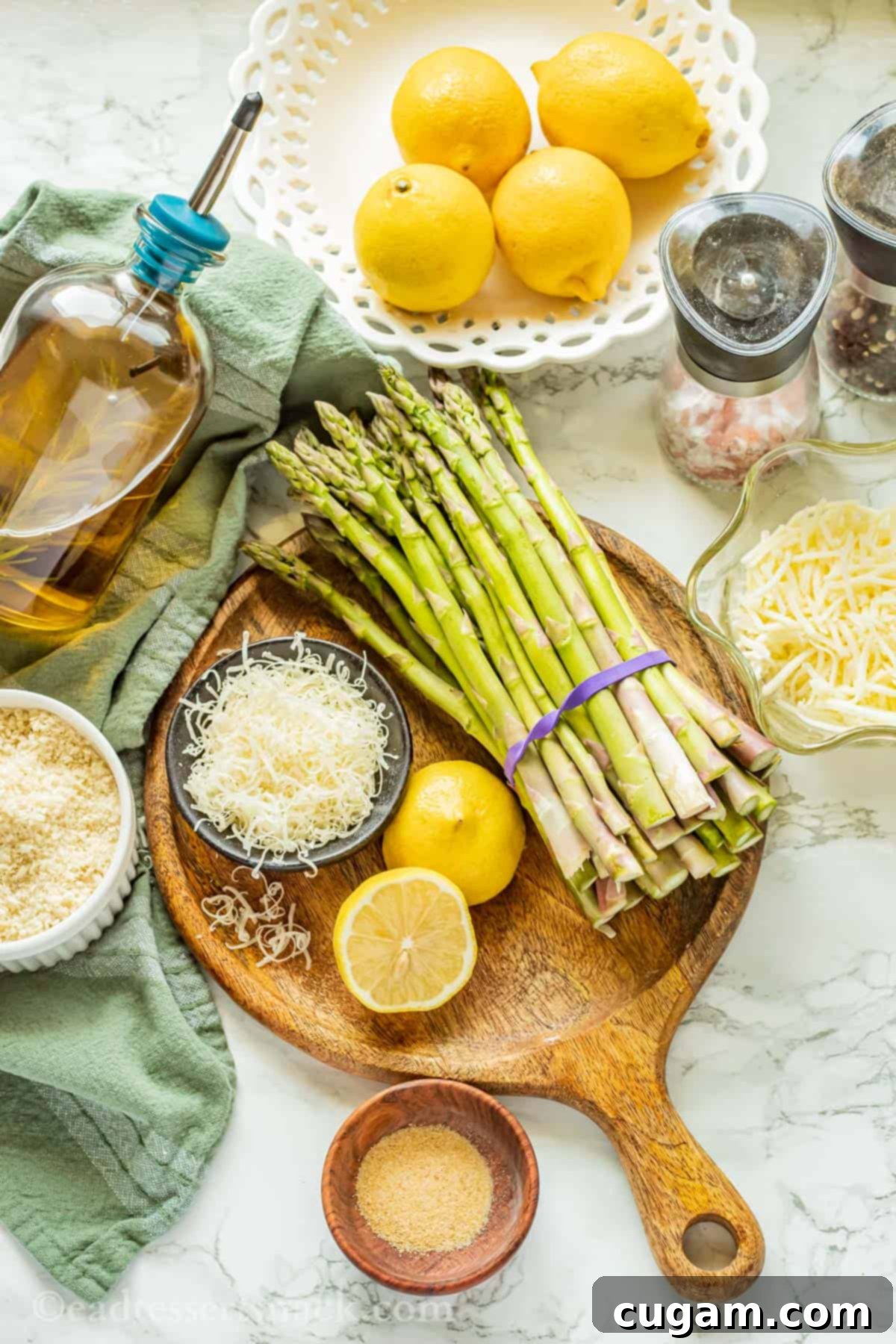 Fresh ingredients for cheesy baked asparagus arranged on a round wooden cutting board with a green towel.