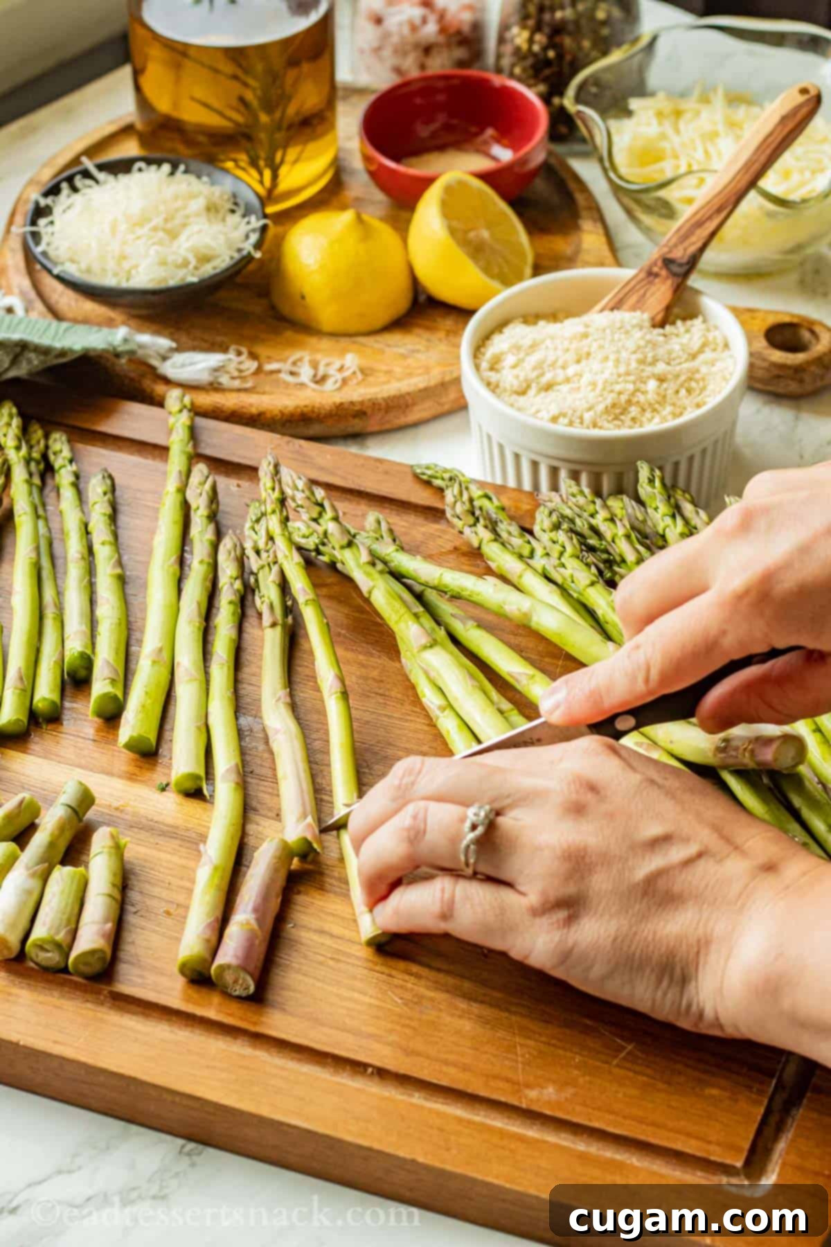 Hands holding a knife, chopping fresh asparagus on a wooden cutting board to remove tough ends.