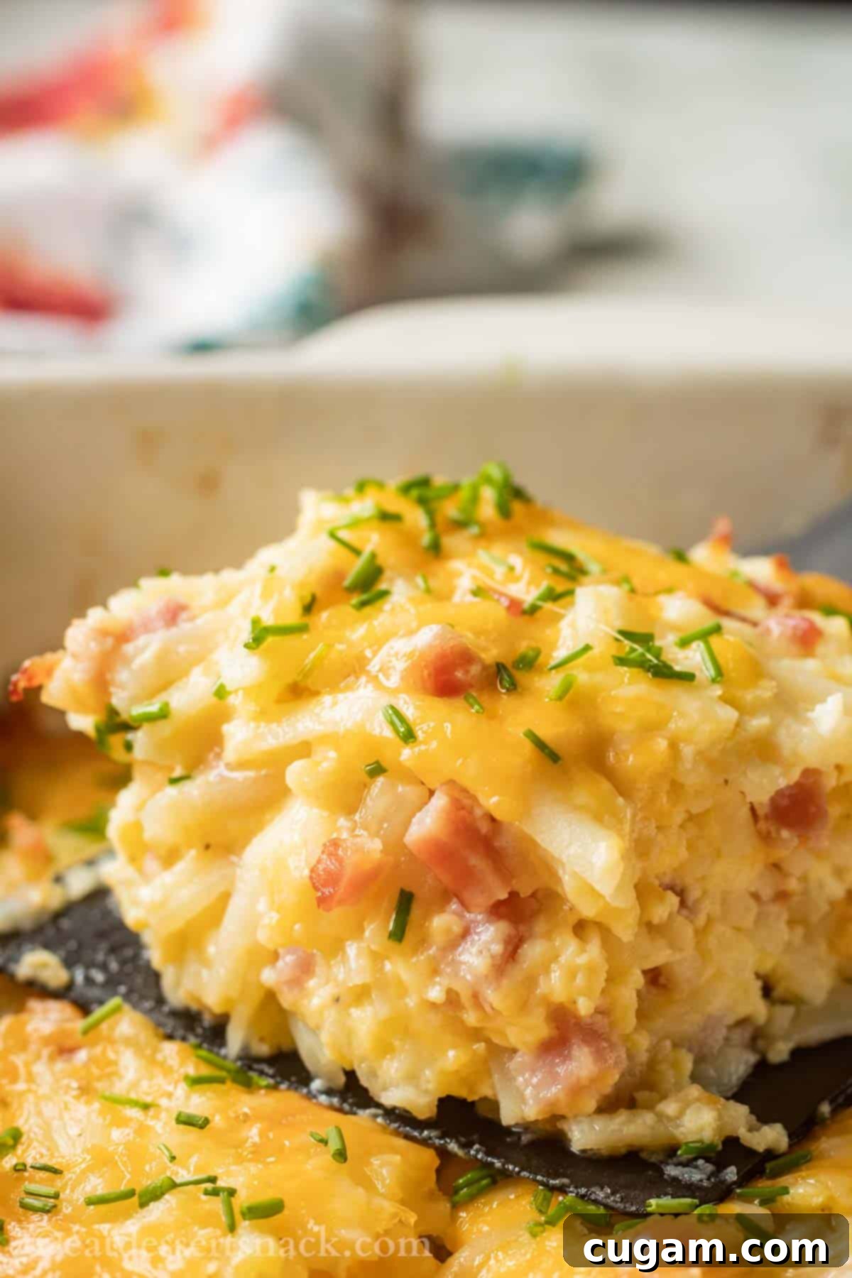 Close up picture of cooked slice of ham and cheese hash brown casserole on black spatula.