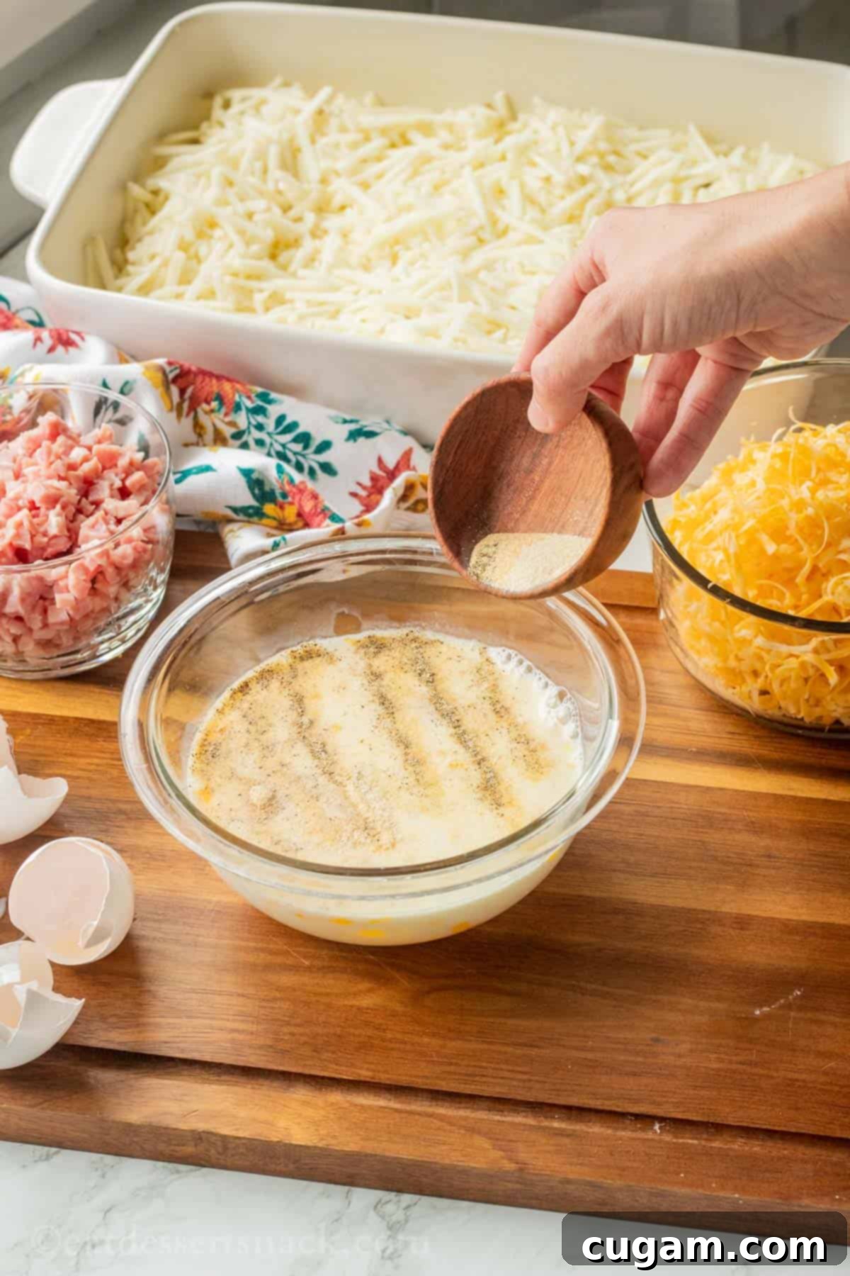 Hand pouring wooden bowl of spices into bowl of egg and milk mixture.