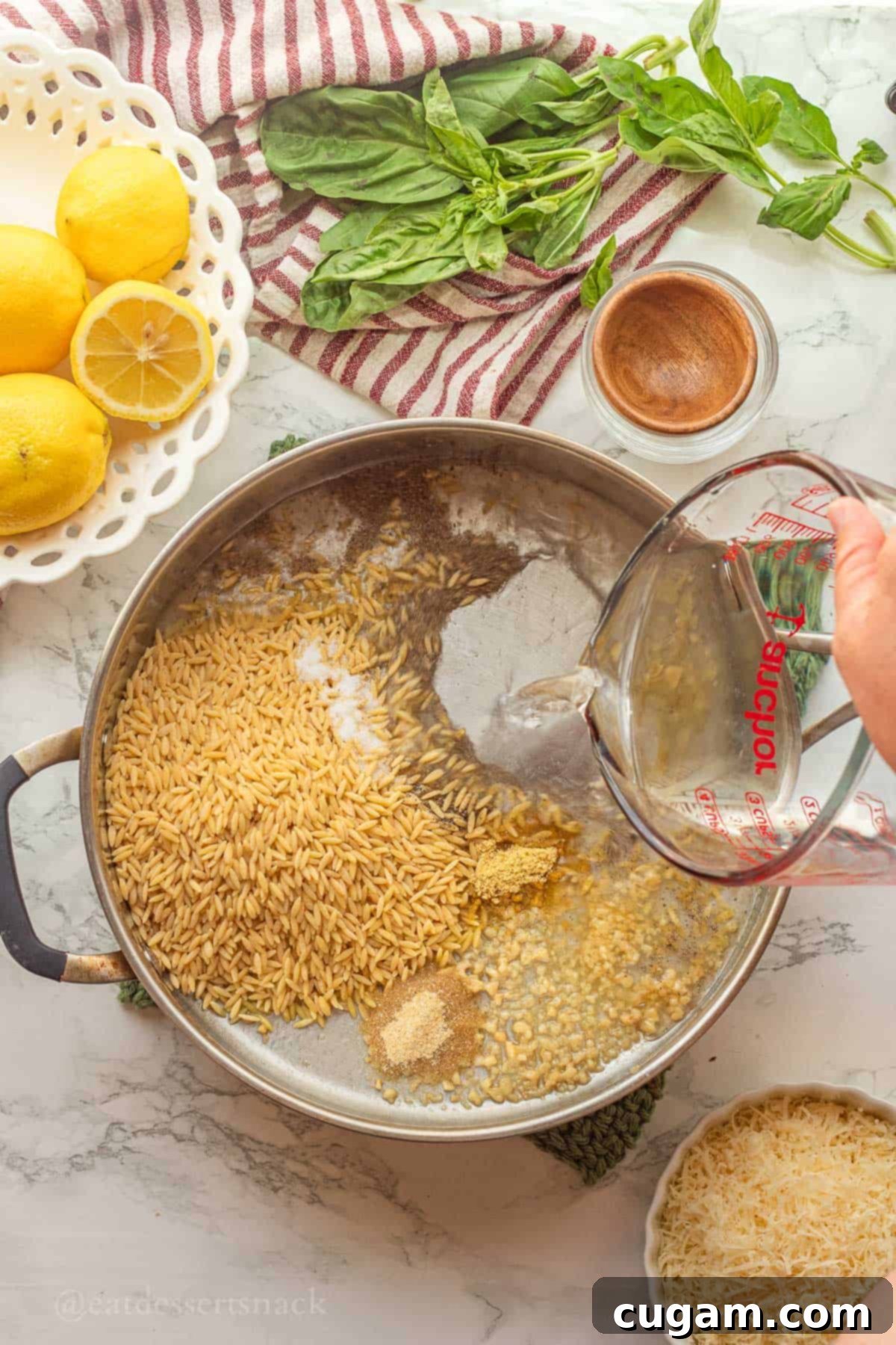 Pouring water into metal pan of raw orzo with spices.