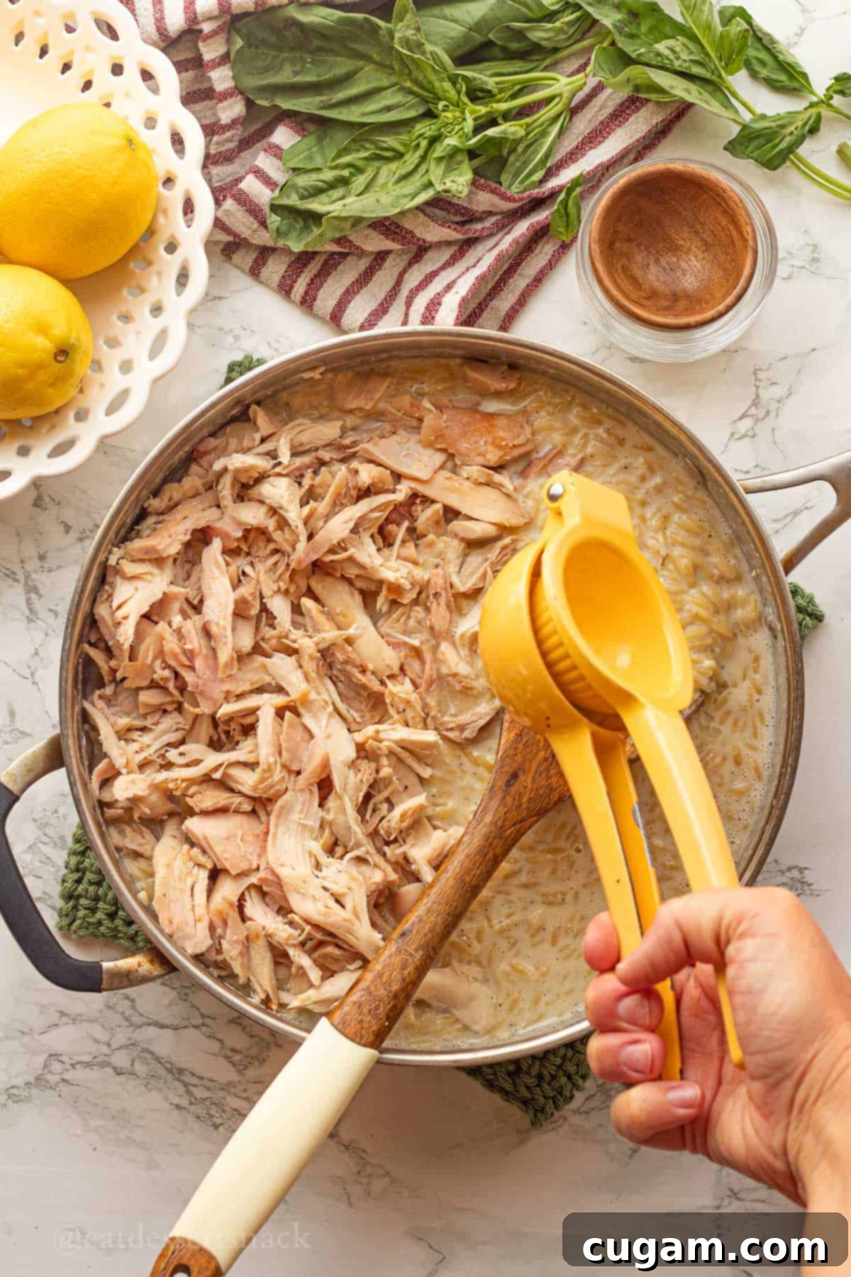 Squeezing lemon juice into pan of chicken and cooked orzo.