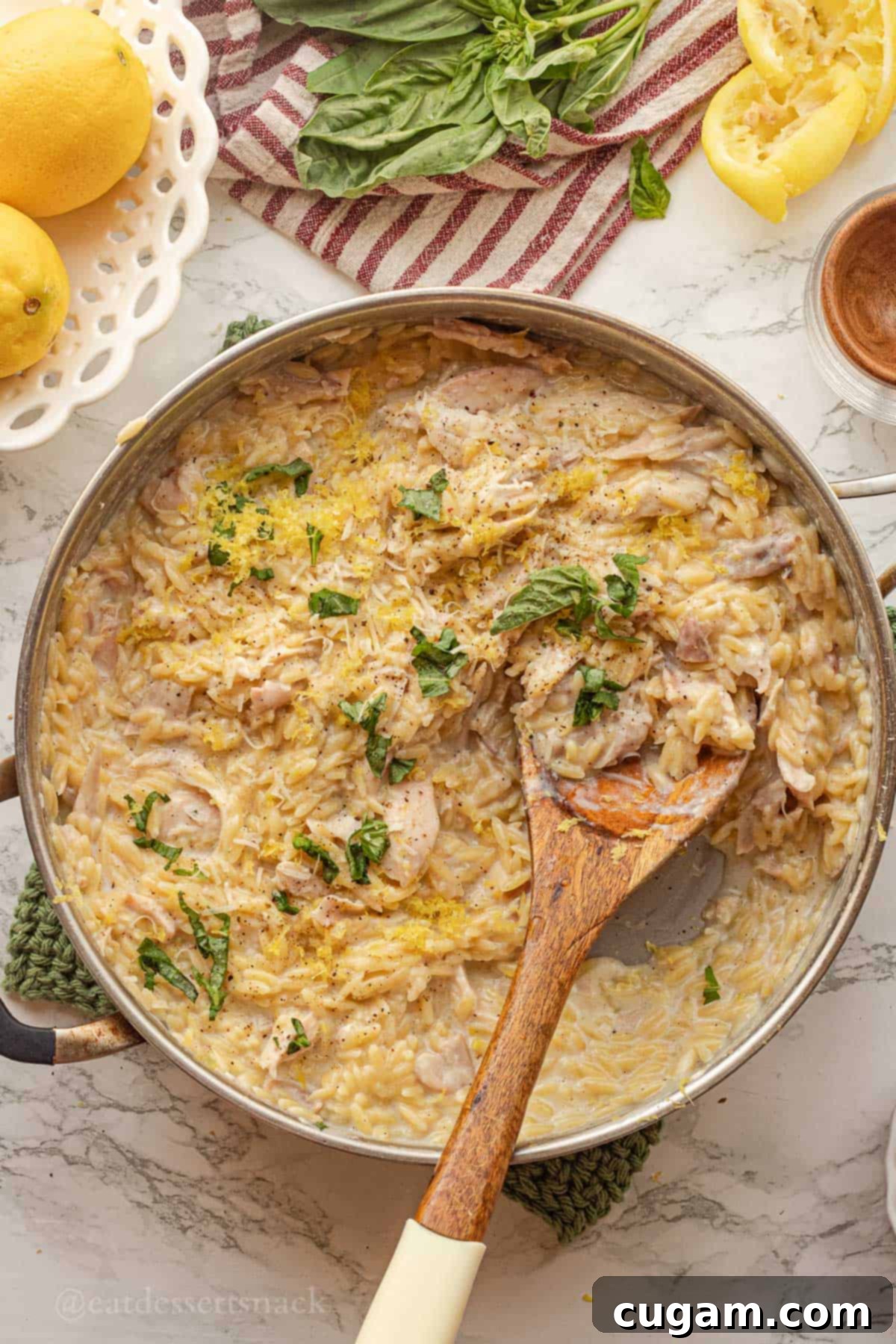 Cooked creamy lemon chicken orzo in metal pan with wppden spoon.