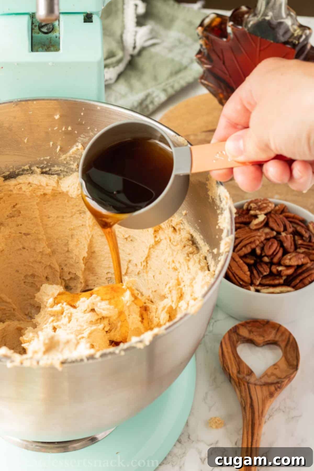 Hand pouring maple syrup into mixing bowl of raw maple cookie dough.