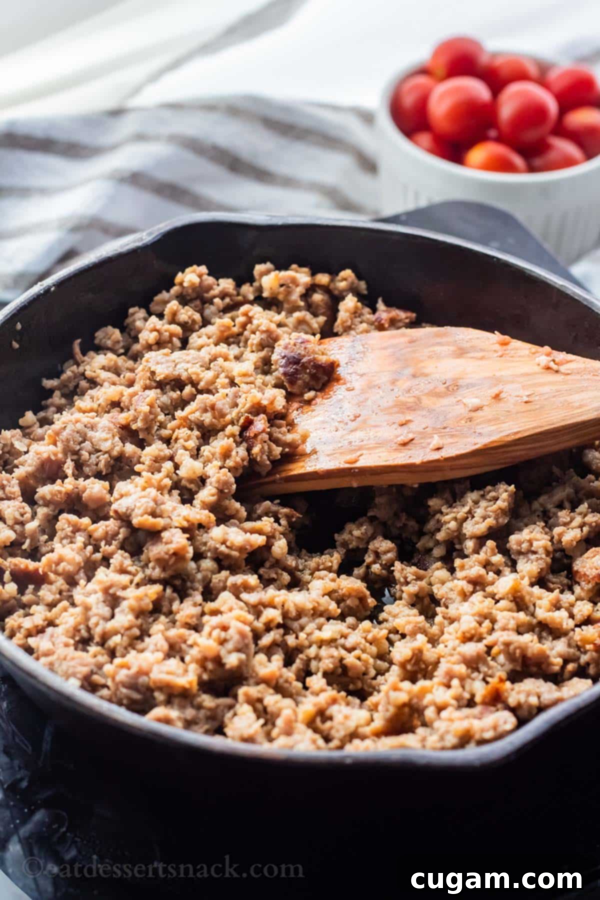 Cooked ground sausage with a rich brown color in a black frying pan, ready to be added to the queso dip ingredients. A wooden spatula rests in the pan.