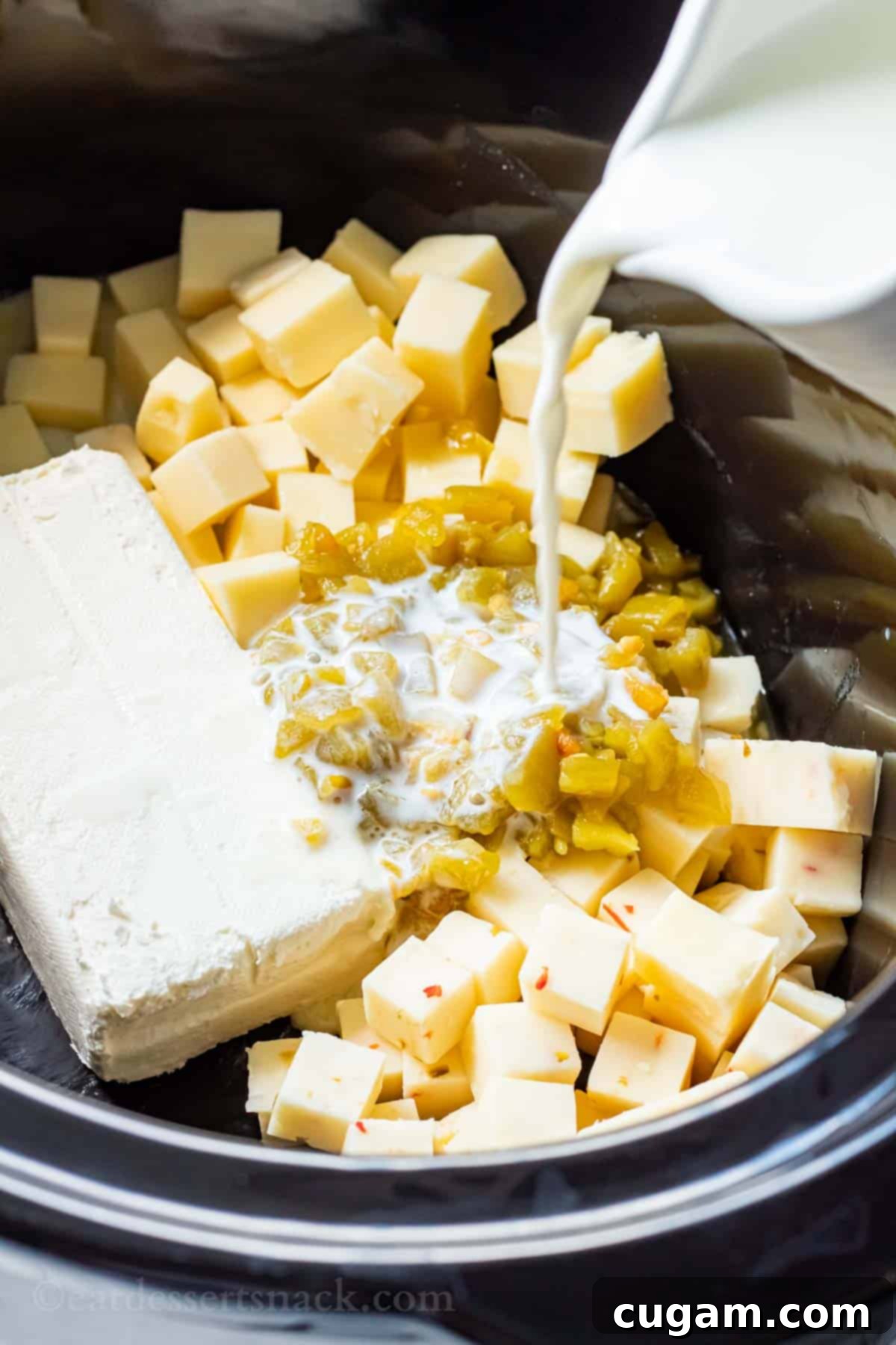 A stream of white milk being poured into a black slow cooker filled with white queso ingredients, including cheese and chiles, preparing for slow melting.