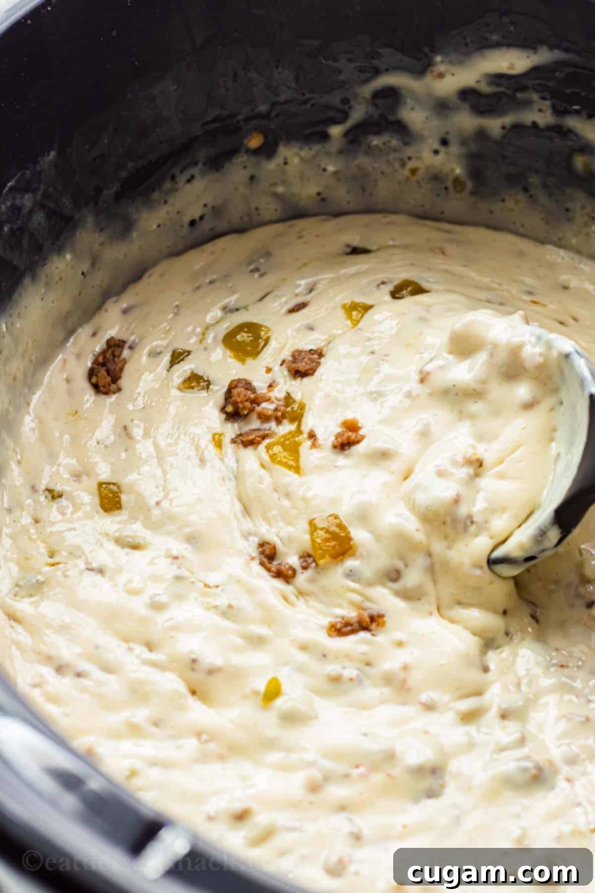 A close-up view of melted, creamy white queso dip bubbling gently in a black slow cooker, ready to be served.