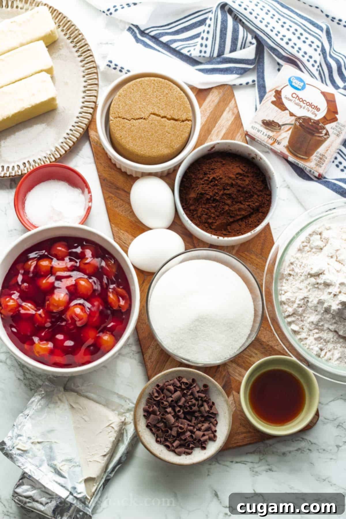 Ingredients for cherry chocolate cheesecake cookies on wood board and marble surface with dish towel.