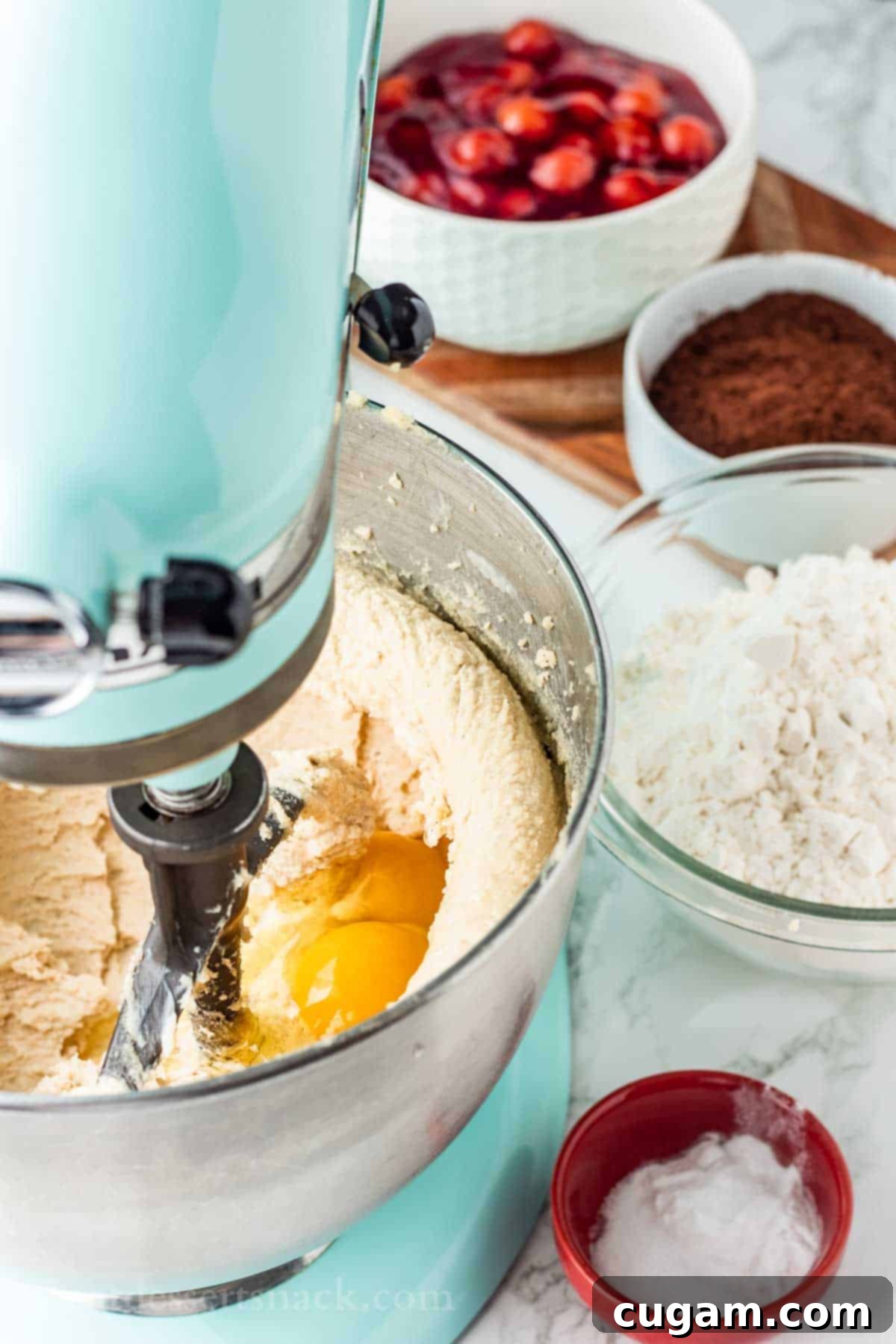 Raw eggs in metal mixing bowl of blue stand mixer with butter and sugar mixture.