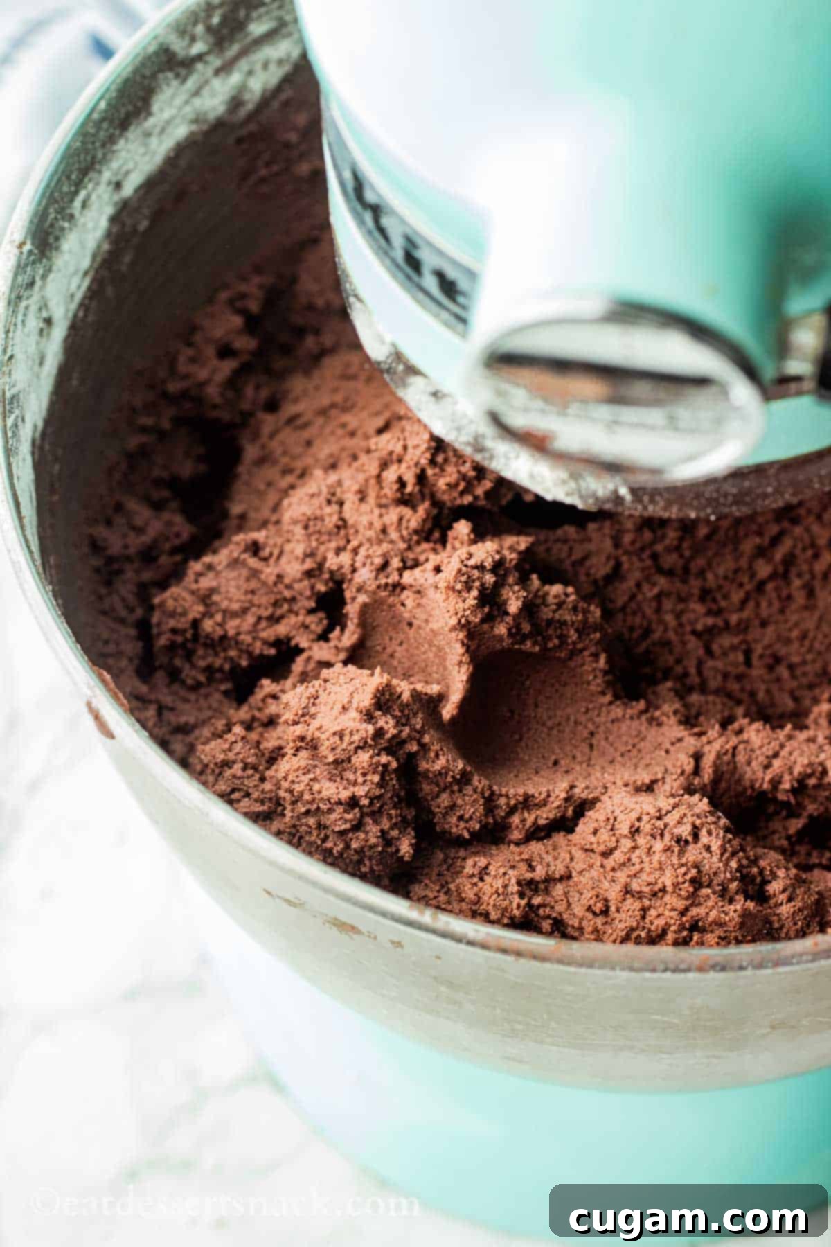 Raw chocolate cookie dough in metal bowl of blue stand mixer.