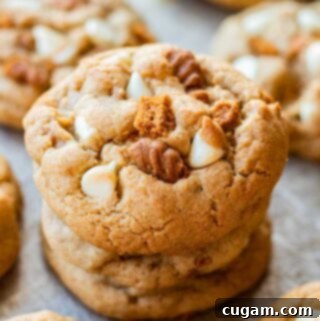 A stack of 3 freshly baked white chocolate biscoff cookies on a metal baking pan, highlighting their soft texture and visible chocolate chips.