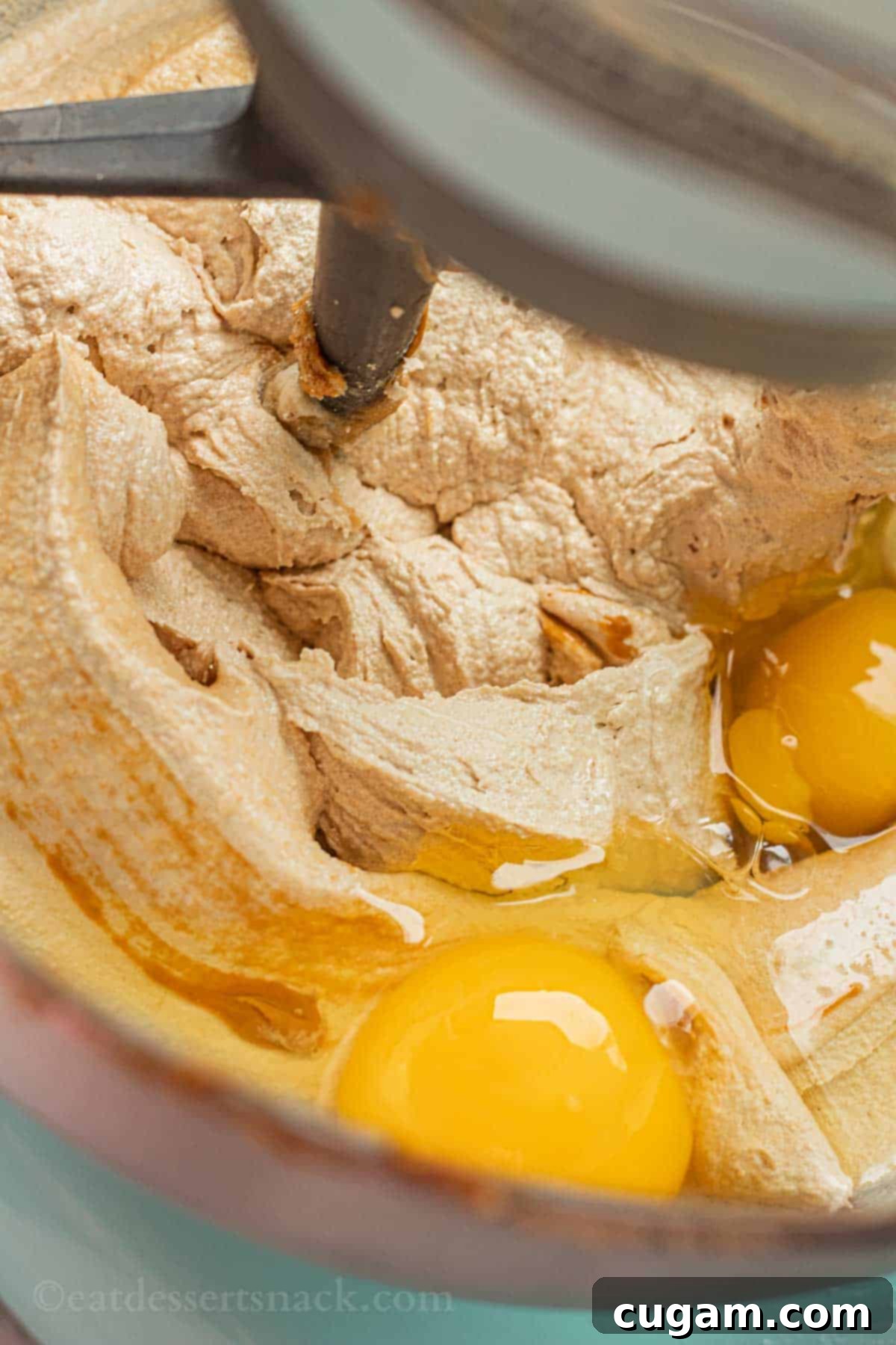 Raw eggs are added to the creamy butter and sugar mixture in a metal mixing bowl, ready to be incorporated into the cookie dough.