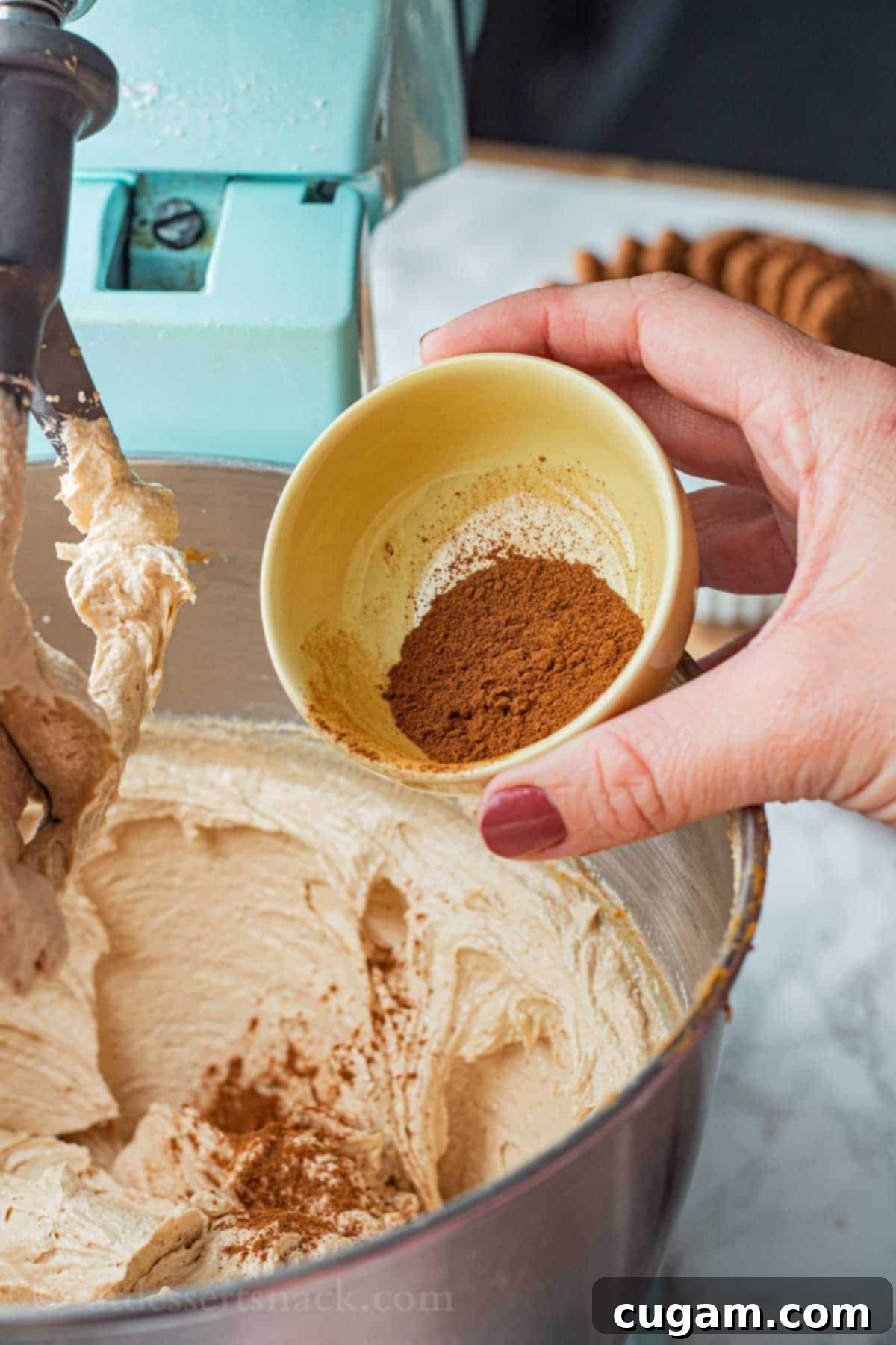 A small yellow bowl of ground cinnamon is poured into a larger bowl of raw cookie dough.