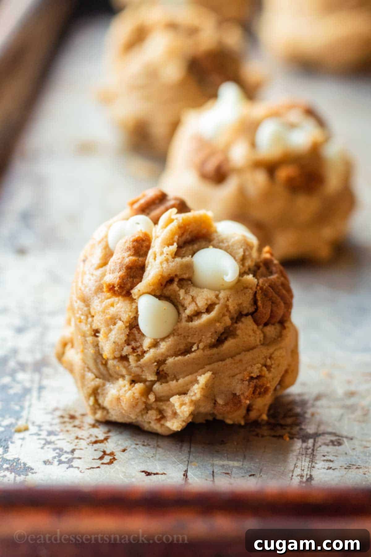 A close-up shot of a raw cookie dough ball, ready for baking, placed on a metal baking sheet.