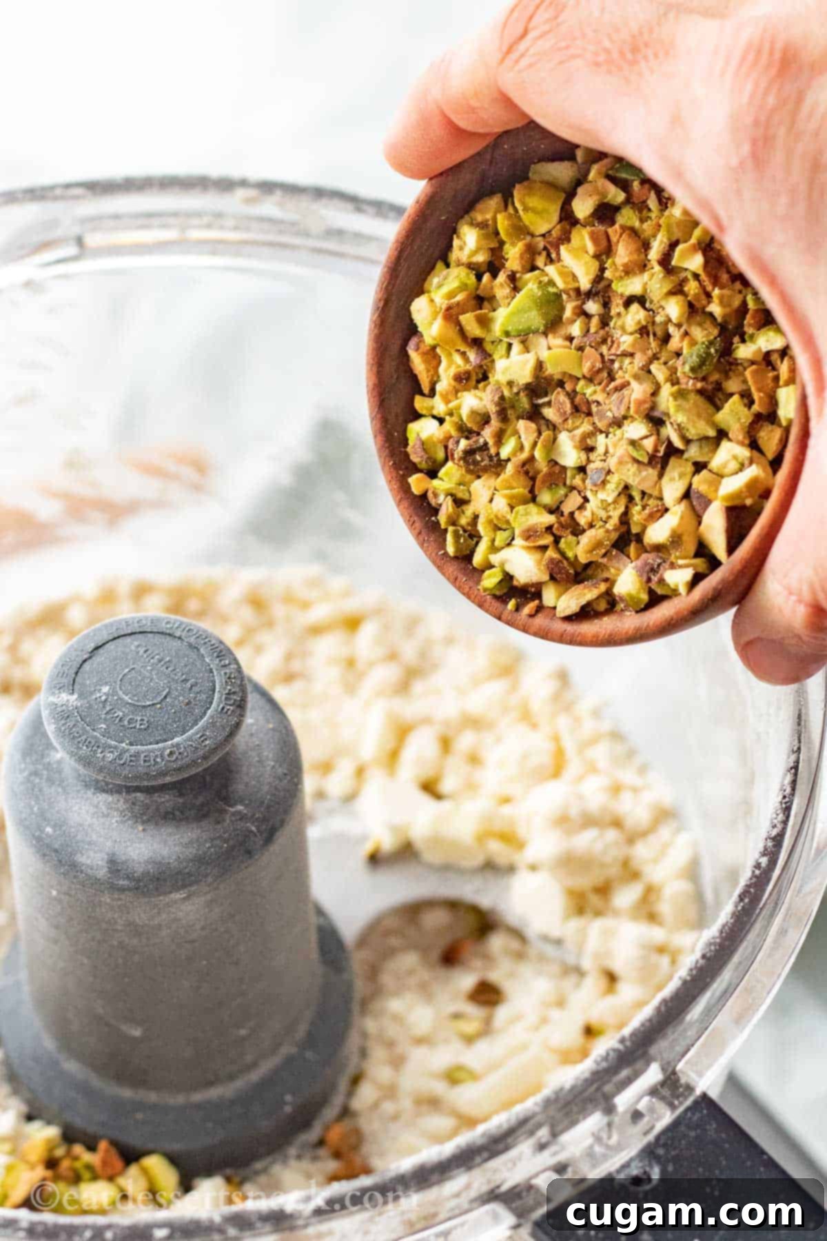 Velvet Pistachio Dream Pie 6 A hand pouring finely chopped pistachios into the flour and butter mixture in a food processor.