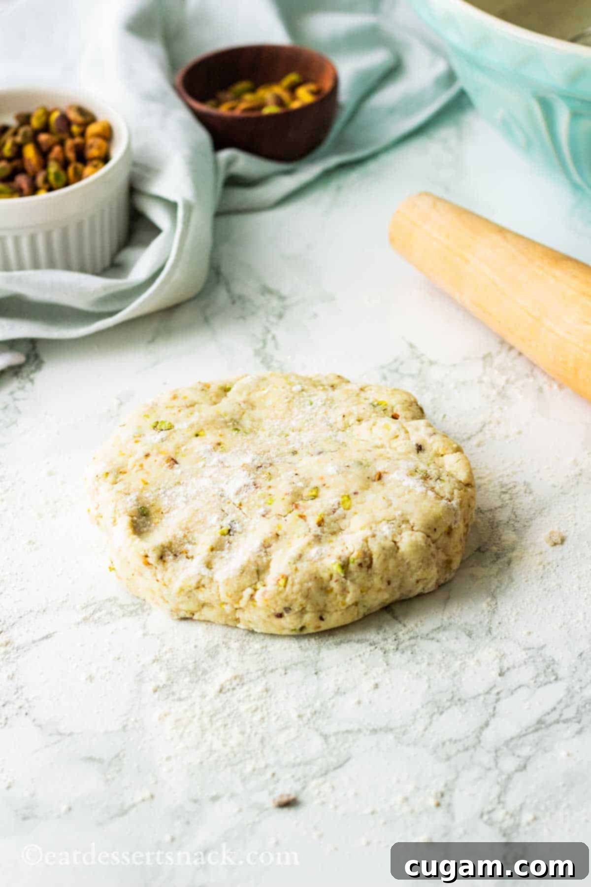 Velvet Pistachio Dream Pie 7 A smooth, disc-shaped pistachio pie dough resting on a marble countertop next to a wooden rolling pin, ready for chilling.