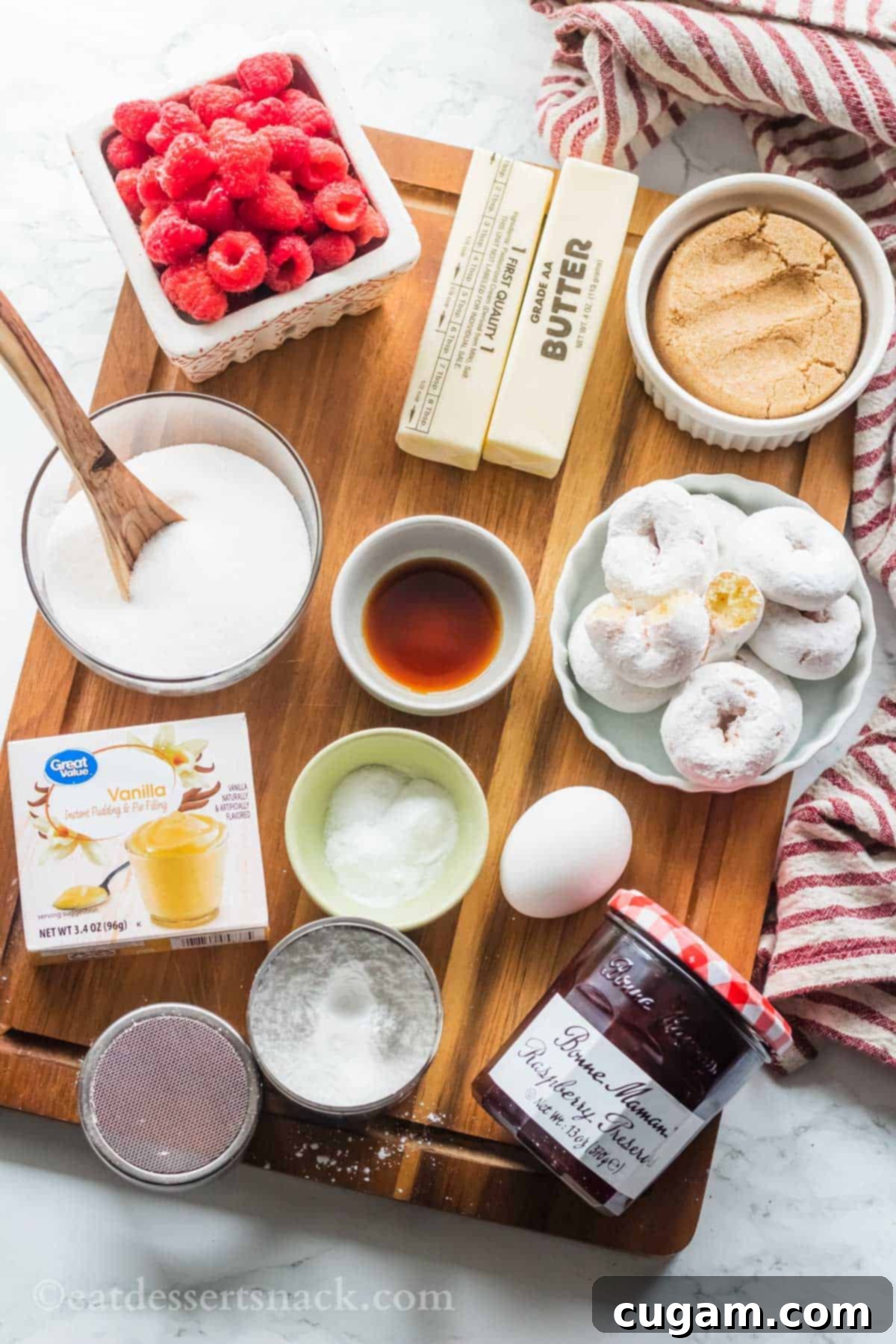 Ingredients for raspberry donut cookies in glass dishes on wood cutting board on marble countertop.