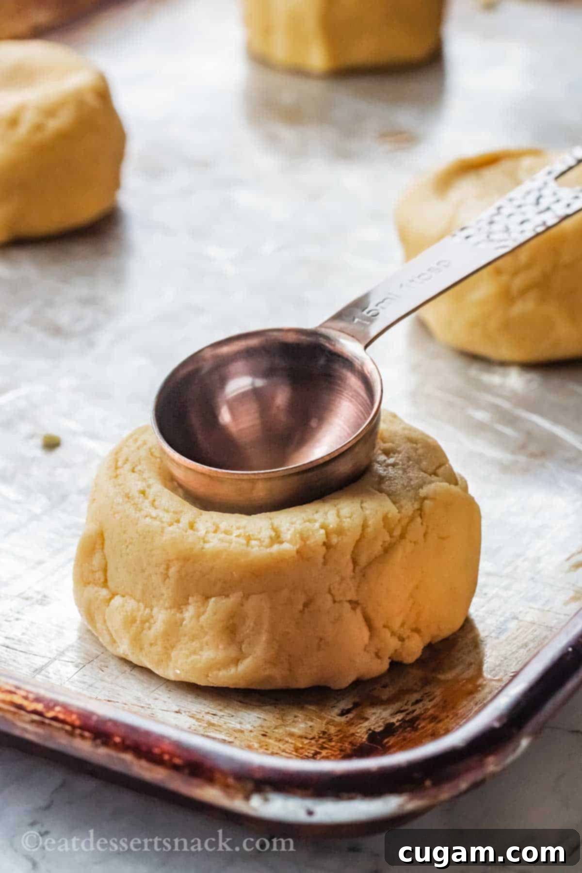 Metal Tablespoon pressing indent into raw cookie dough on metal pan.