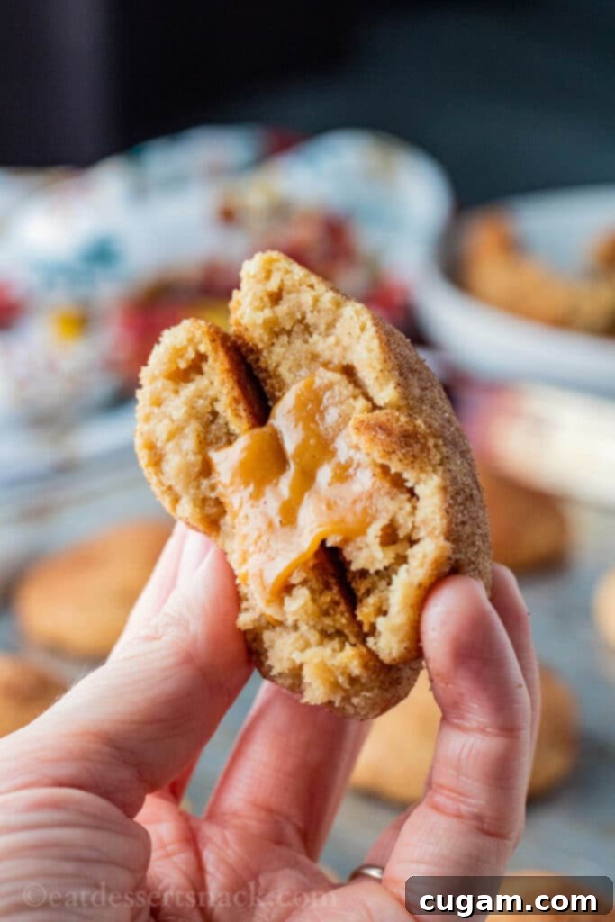 Baked caramel stuffed snickerdoodle broken in half in hand, showing molten caramel inside.