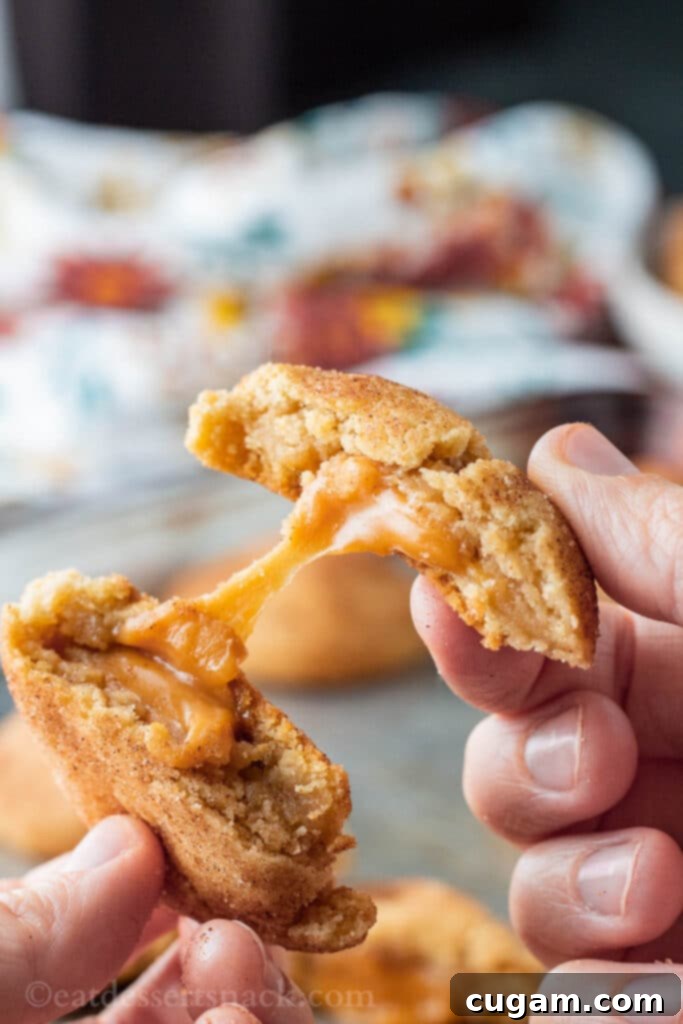 Hands pulling a warm caramel stuffed snickerdoodle apart, revealing the stretchy, molten caramel center.