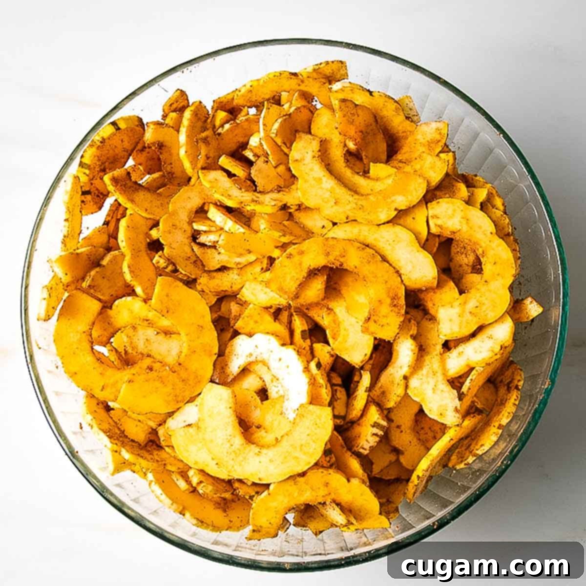 Glass bowl filled with spiced delicata half moon thin slices, ready for roasting.
