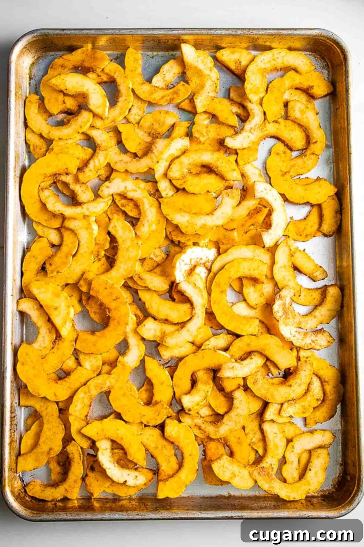 Single layer of half moon shaped winter squash arranged on a baking tray before roasting.