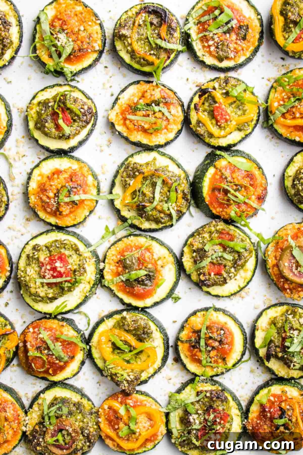 Quick Zucchini Pizza Bites 2 Rows of zucchini slices, topped with red or green sauce and various vegetable toppings to create mini pizzas. All are sprinkled with vegan parmesan and fresh basil.