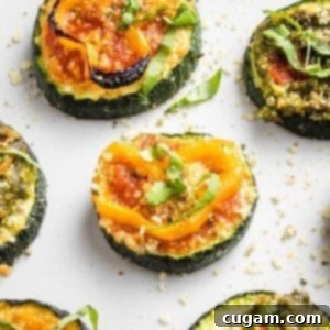 Quick Zucchini Pizza Bites 13 Close up of a few sliced zucchini pizza bites on a white tray. One has red sauce, a sliced yellow pepper and some fesh basil, another has pesto and roasted red pepper.