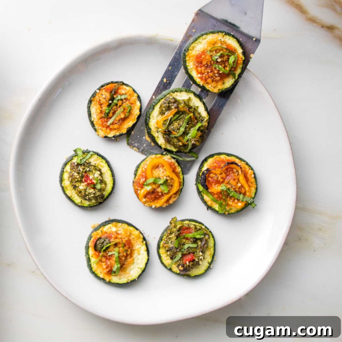 Close-up of baked zucchini pizza bites arranged artfully on a white platter, ready for serving.