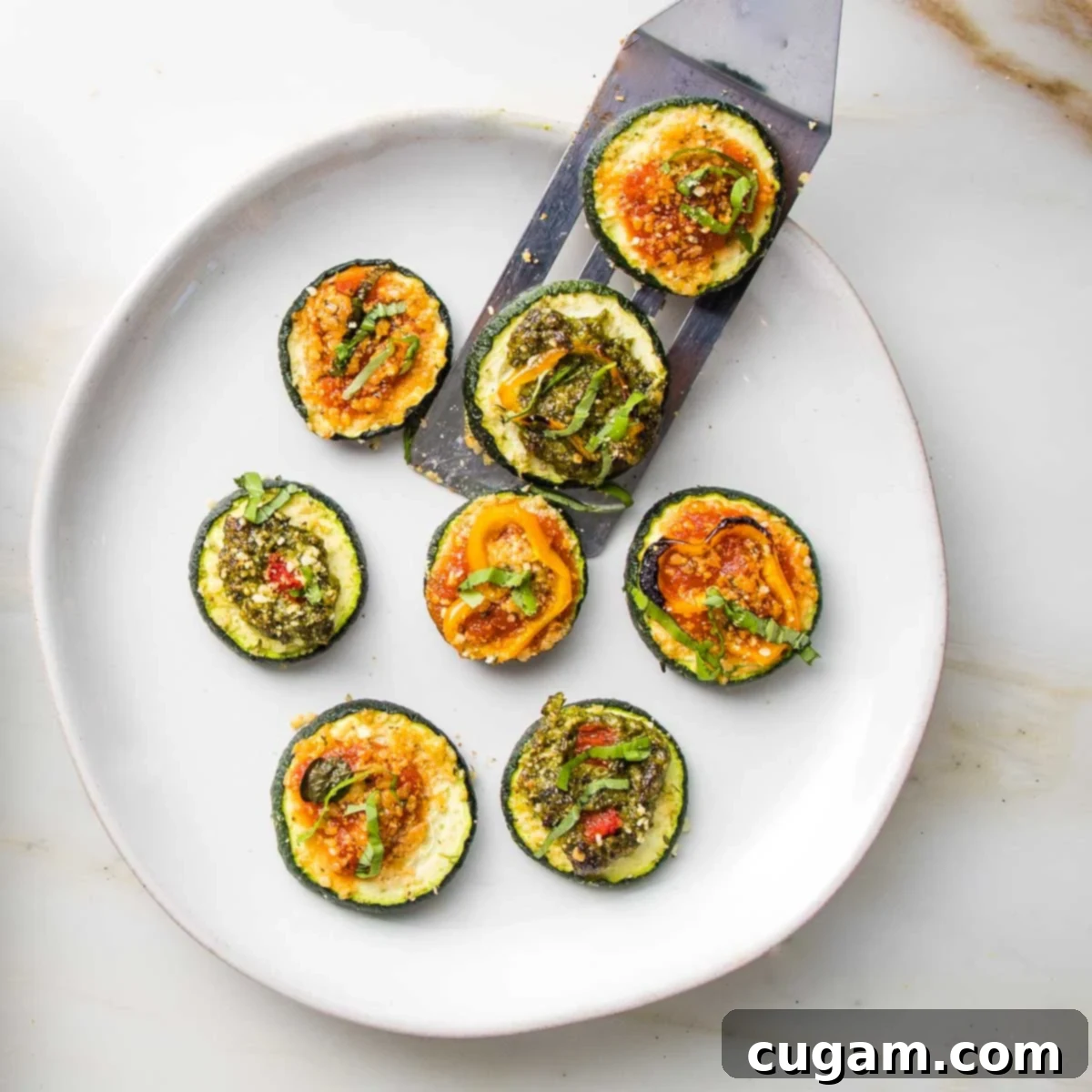 Quick Zucchini Pizza Bites 3 A close-up shot of multiple zucchini pizza bites on a white plate, garnished with fresh basil.