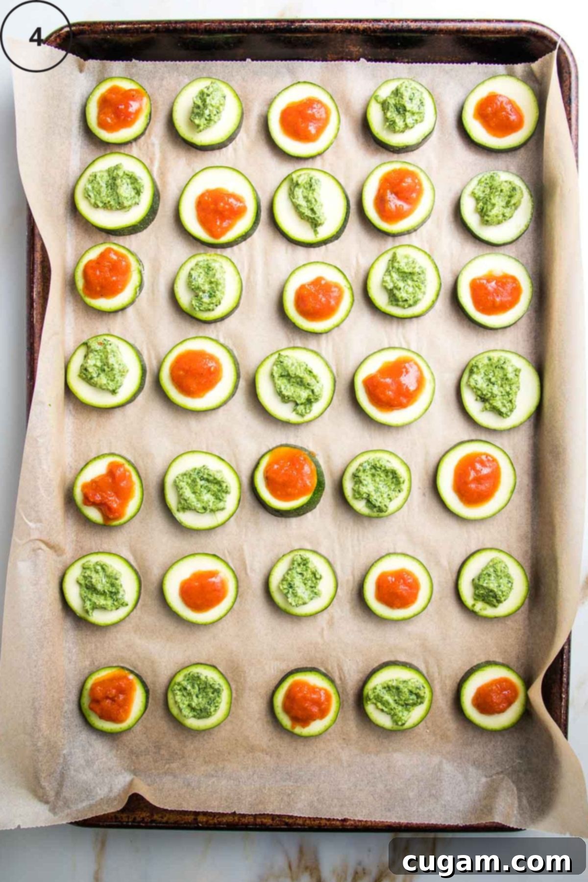 Baking tray with rows of sliced zucchini rounds topped with marinara or pesto.