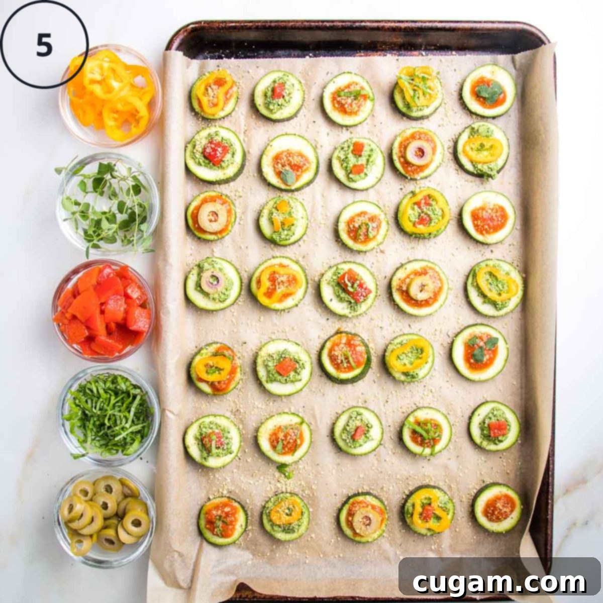 Baking tray of zucchini pizza bites with small dishes on the side with toppings.