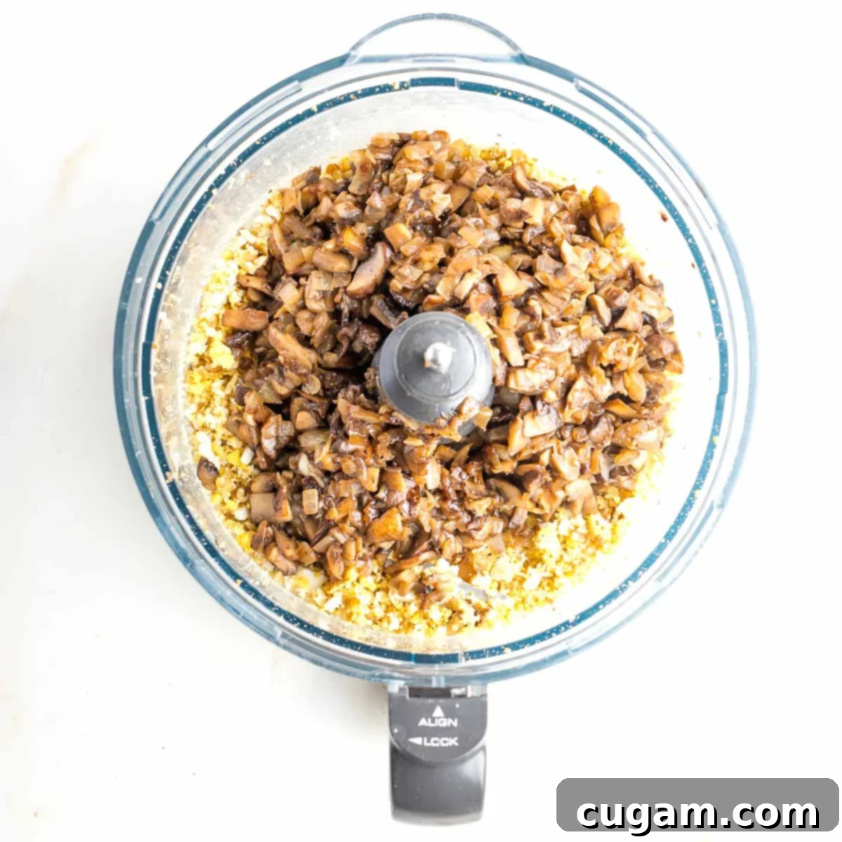 The food processor bowl holds a mixture of pulsed hard-boiled eggs and walnuts, with the freshly sautéed, caramelized onions and mushrooms piled on top, ready for final blending into mock chopped liver.