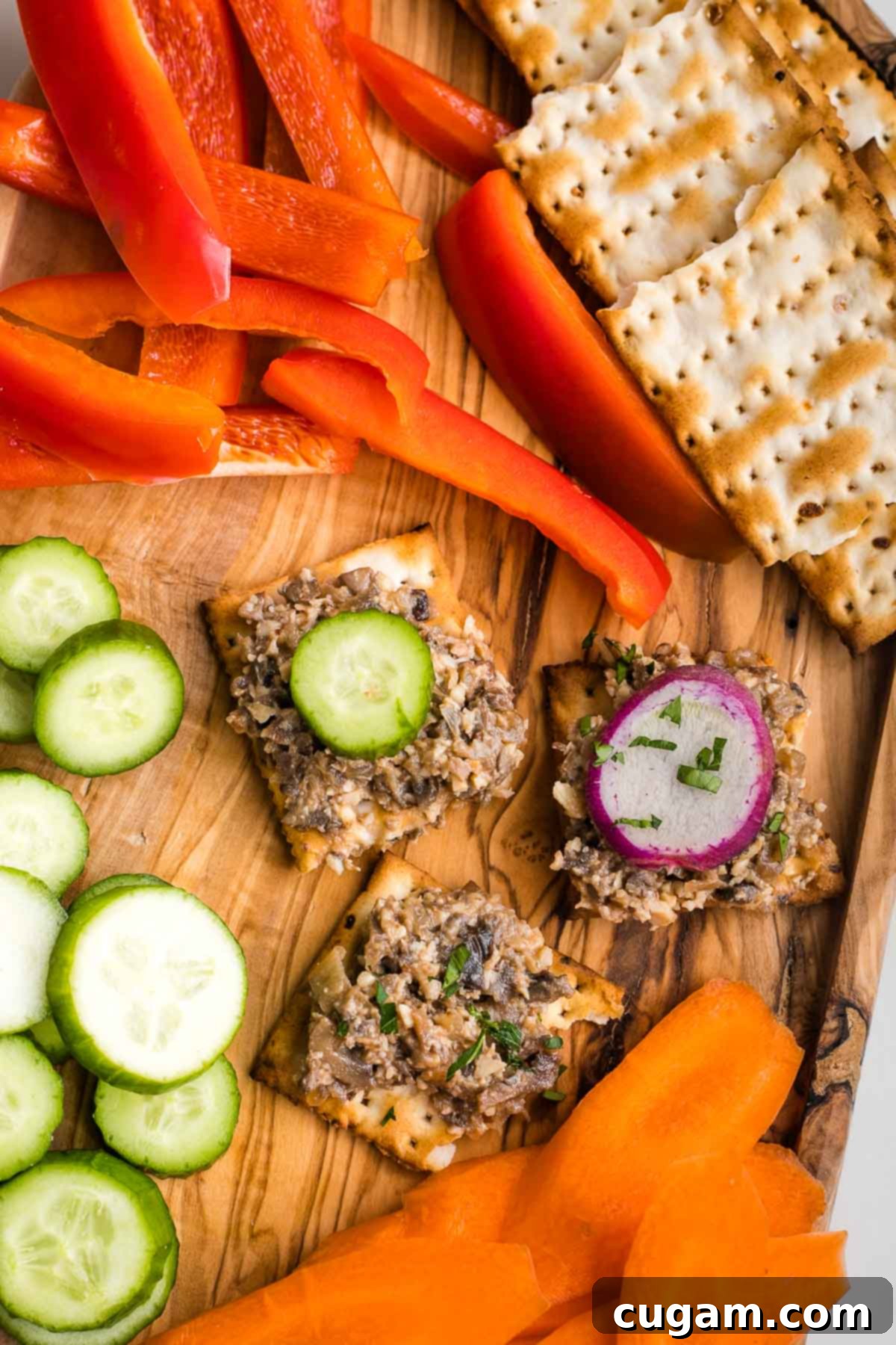 A rustic wooden board laden with an array of vibrant raw vegetables, including bell peppers and carrots, alongside crispy matzah crackers generously spread with delicious mock chopped liver, creating an inviting appetizer platter.