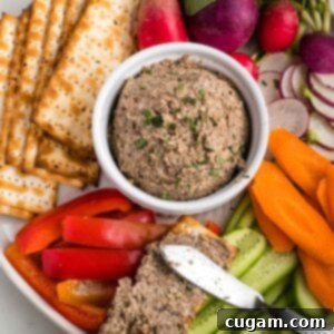 Vegetarian chopped liver in a bowl surrounded by matzo crackers and raw vegetables.