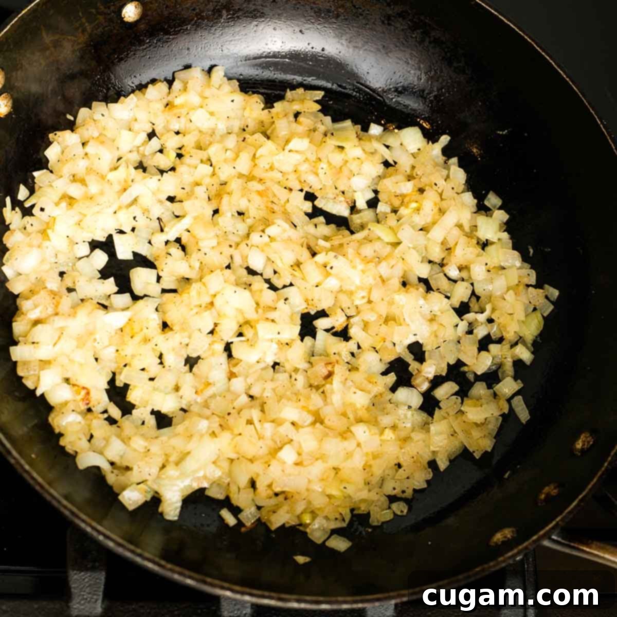 A cast iron skillet filled with diced onions, glistening as they sauté and soften over medium-low heat, with slight browning visible at the edges.