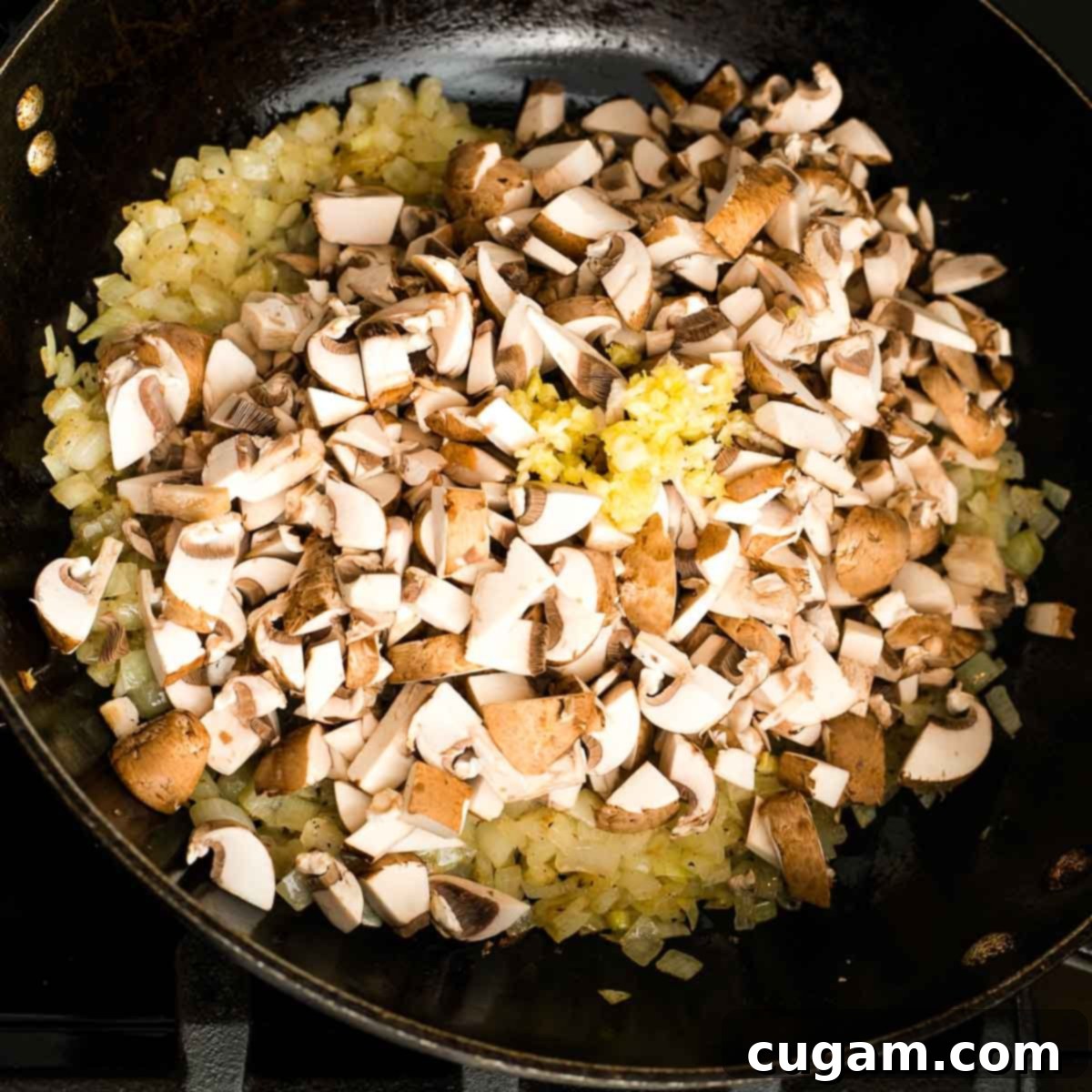 A close-up of diced onions sautéing in a dark pan, becoming translucent and slightly browned, with steam gently rising, preparing the flavor base.