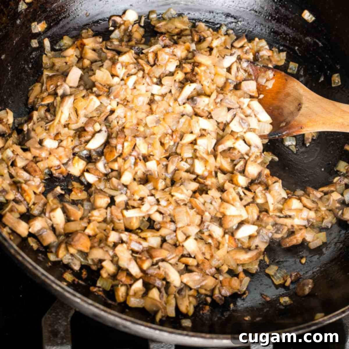 A wide shot of a skillet filled with sautéing diced onions and chopped mushrooms, browning beautifully together, indicating they are almost ready to be blended for the mock chopped liver.