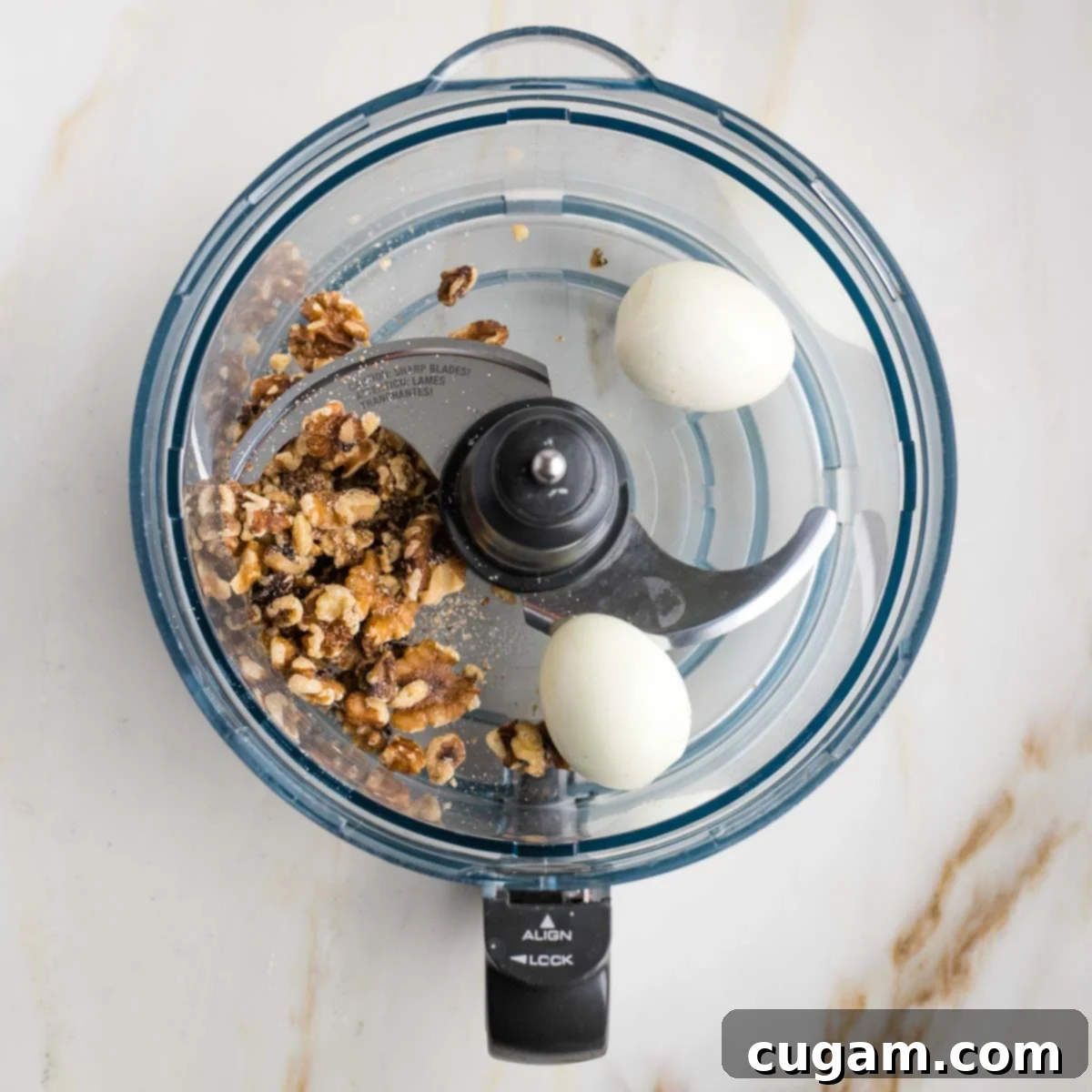 The bowl of a food processor containing whole walnuts and two peeled, large hard-boiled eggs, poised to be pulsed into a chunky mixture.