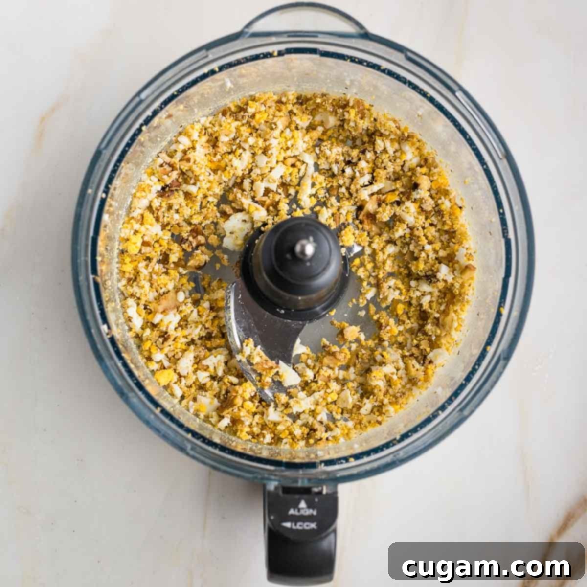 A close-up shot inside a food processor bowl, showing finely pulsed walnuts and hard-boiled eggs, creating a coarse, crumbly texture ideal for the mock chopped liver base.